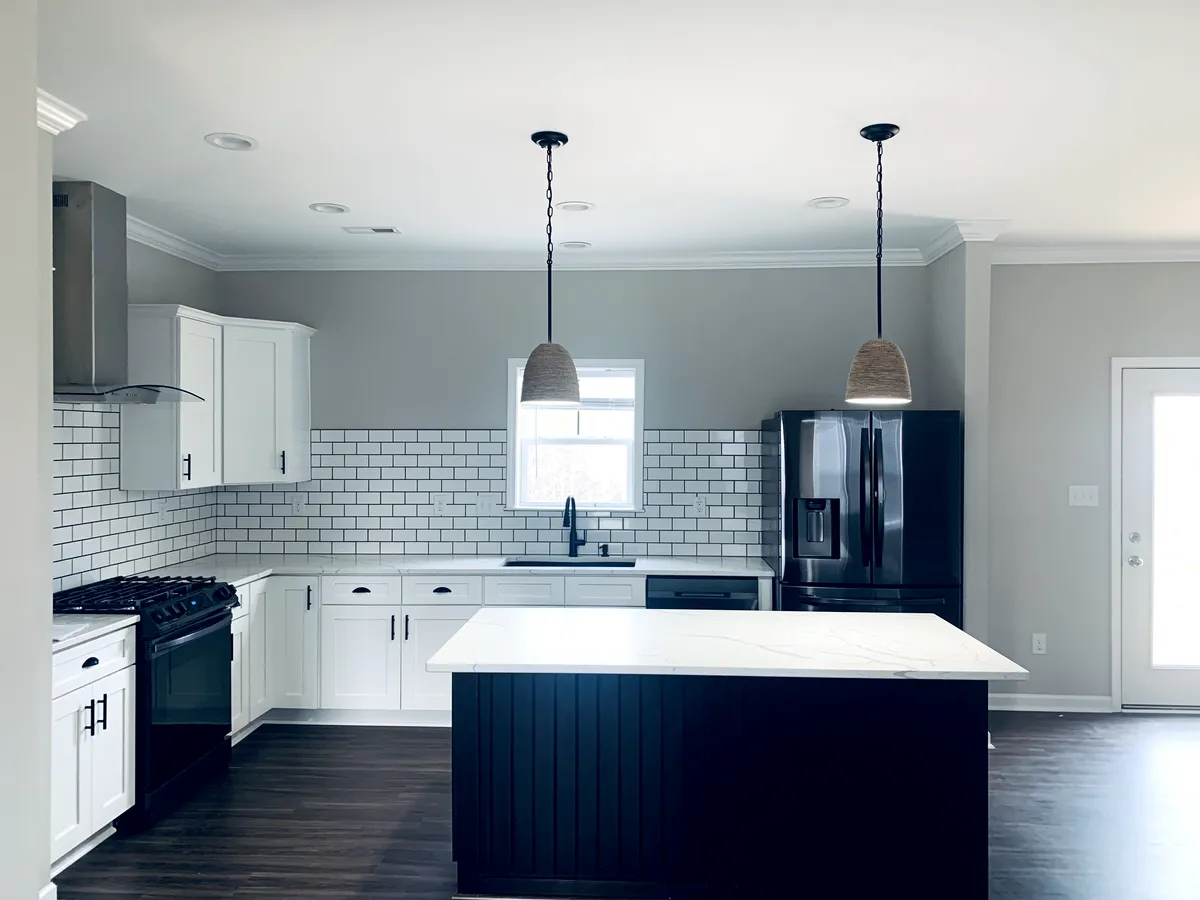 Modern kitchen with white cabinets, dark island, black appliances, and pendant lights.