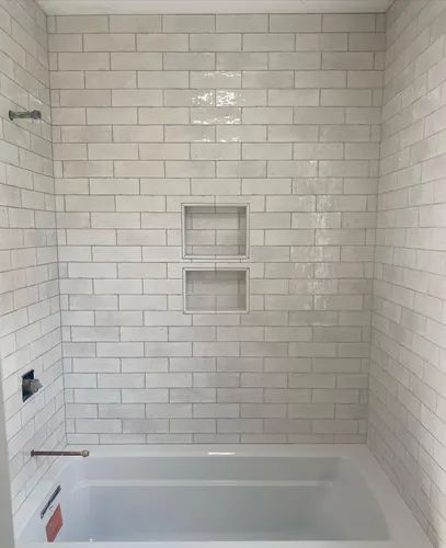 White tiled shower with a bathtub, two built-in shelves, and a silver showerhead.