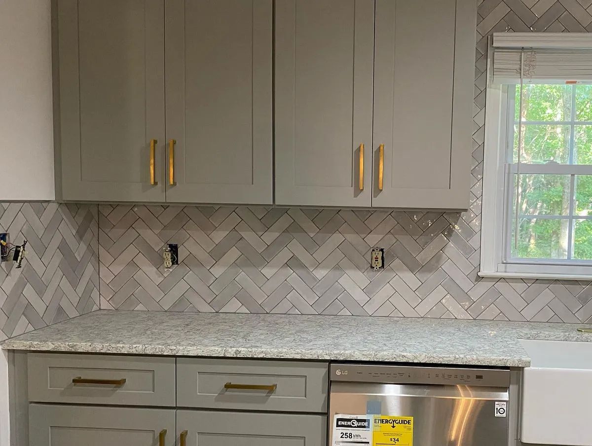 Gray kitchen cabinets with gold hardware and herringbone tile backsplash.