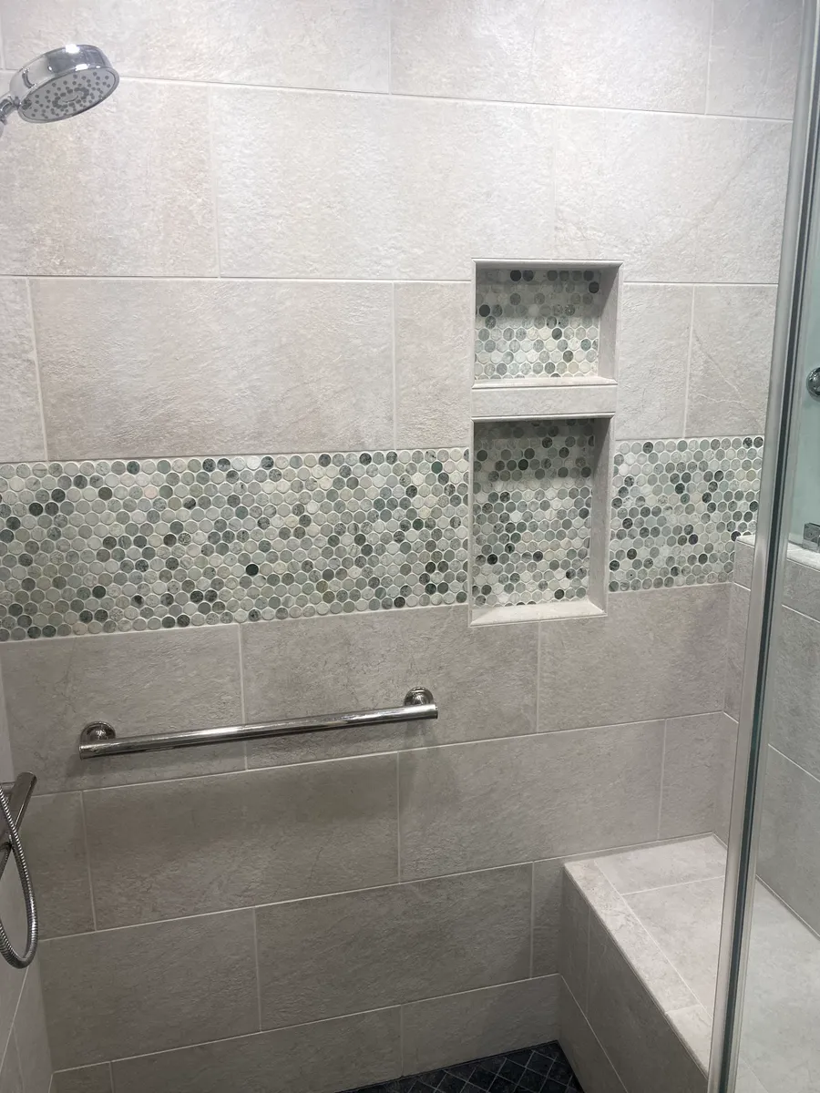 Shower with light beige tile, pebble accent, two built-in shelves, grab bar, and bench seat.