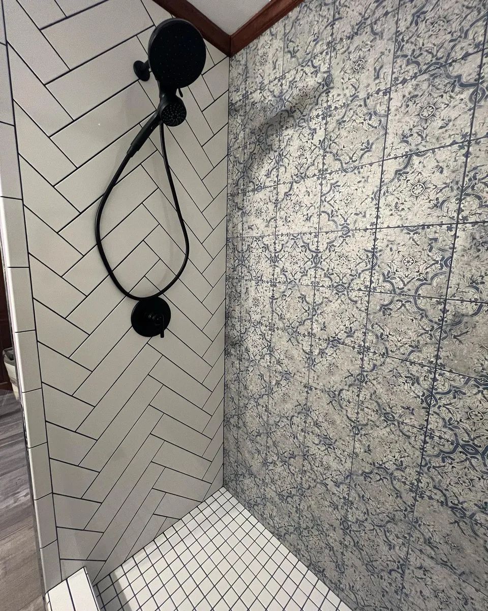 Shower with white herringbone tile and patterned wall tile. Black showerhead and fixtures.