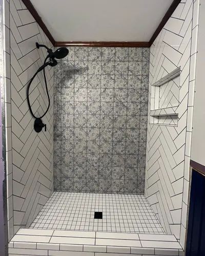 Shower with white herringbone tile walls and patterned tile back wall, black fixtures, and built-in shelves.