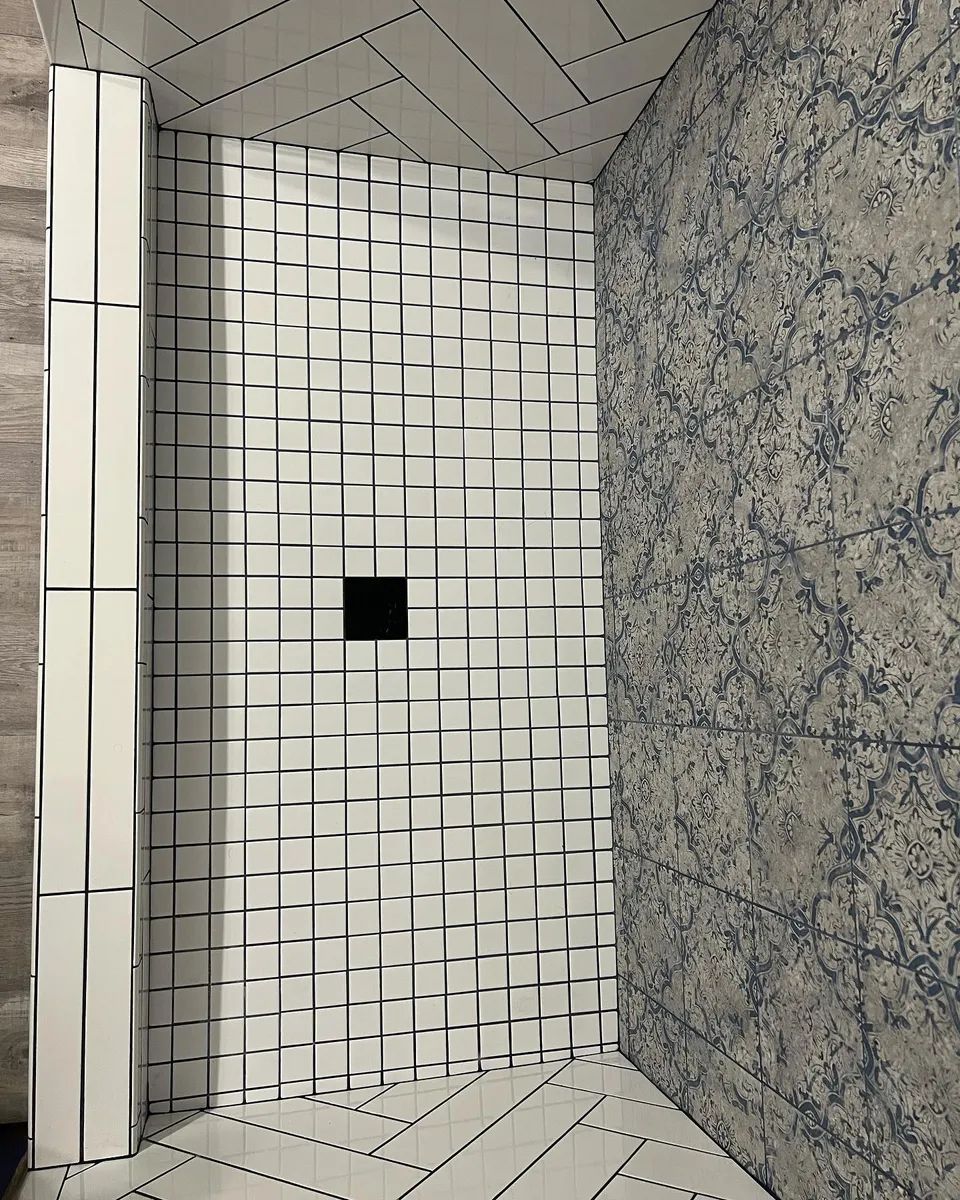Shower interior with textured white tile walls, a blue and gray patterned wall, and a black square shower drain.