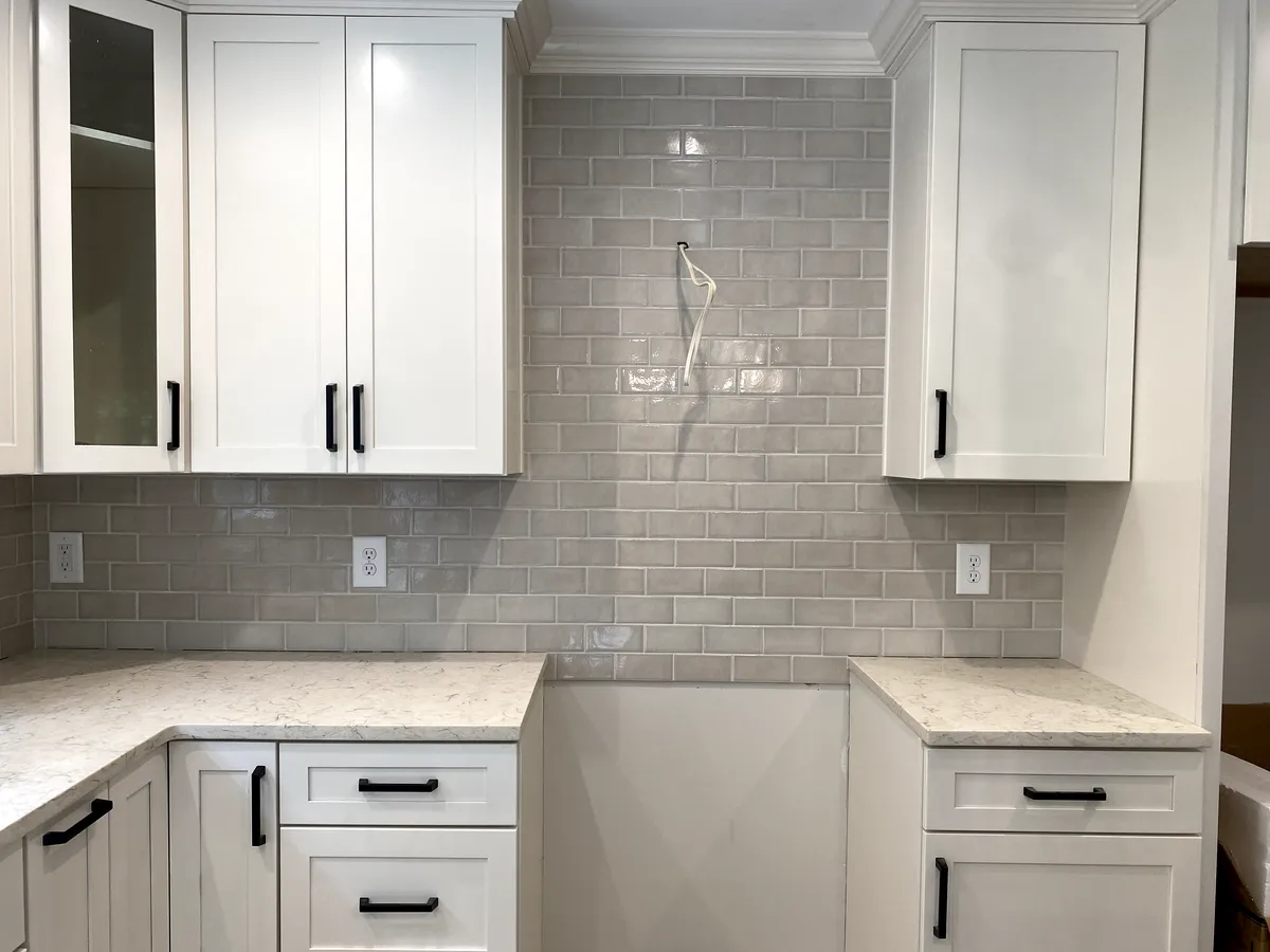 White kitchen cabinets with light gray subway tile backsplash and speckled countertops.