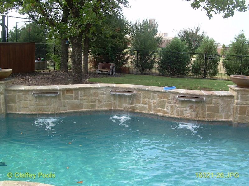 A swimming pool with a stone wall and a waterfall
