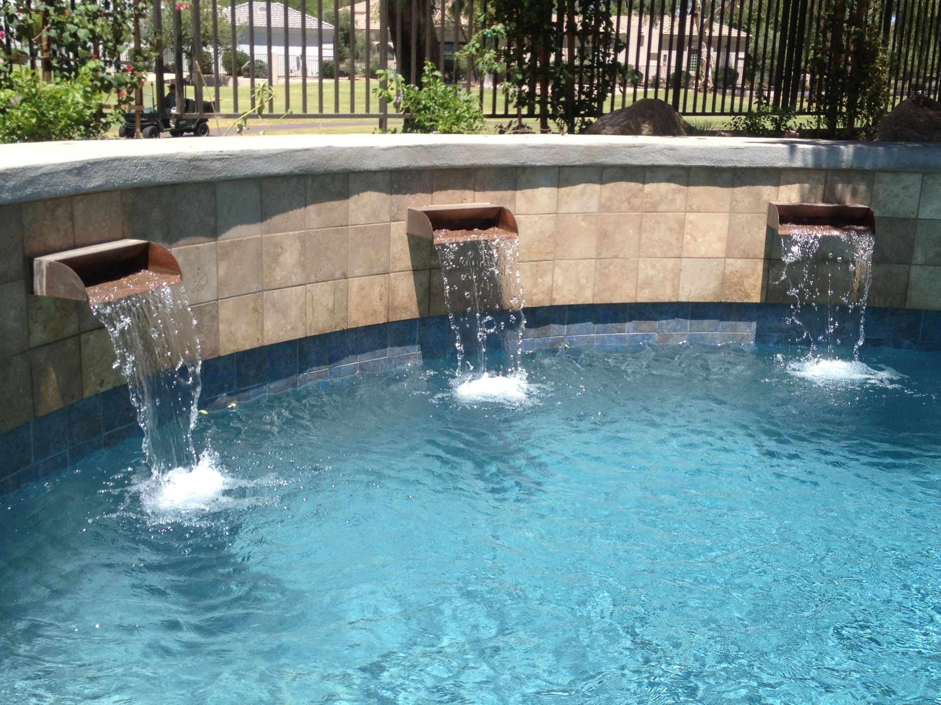 Three waterfalls in a swimming pool with a fence