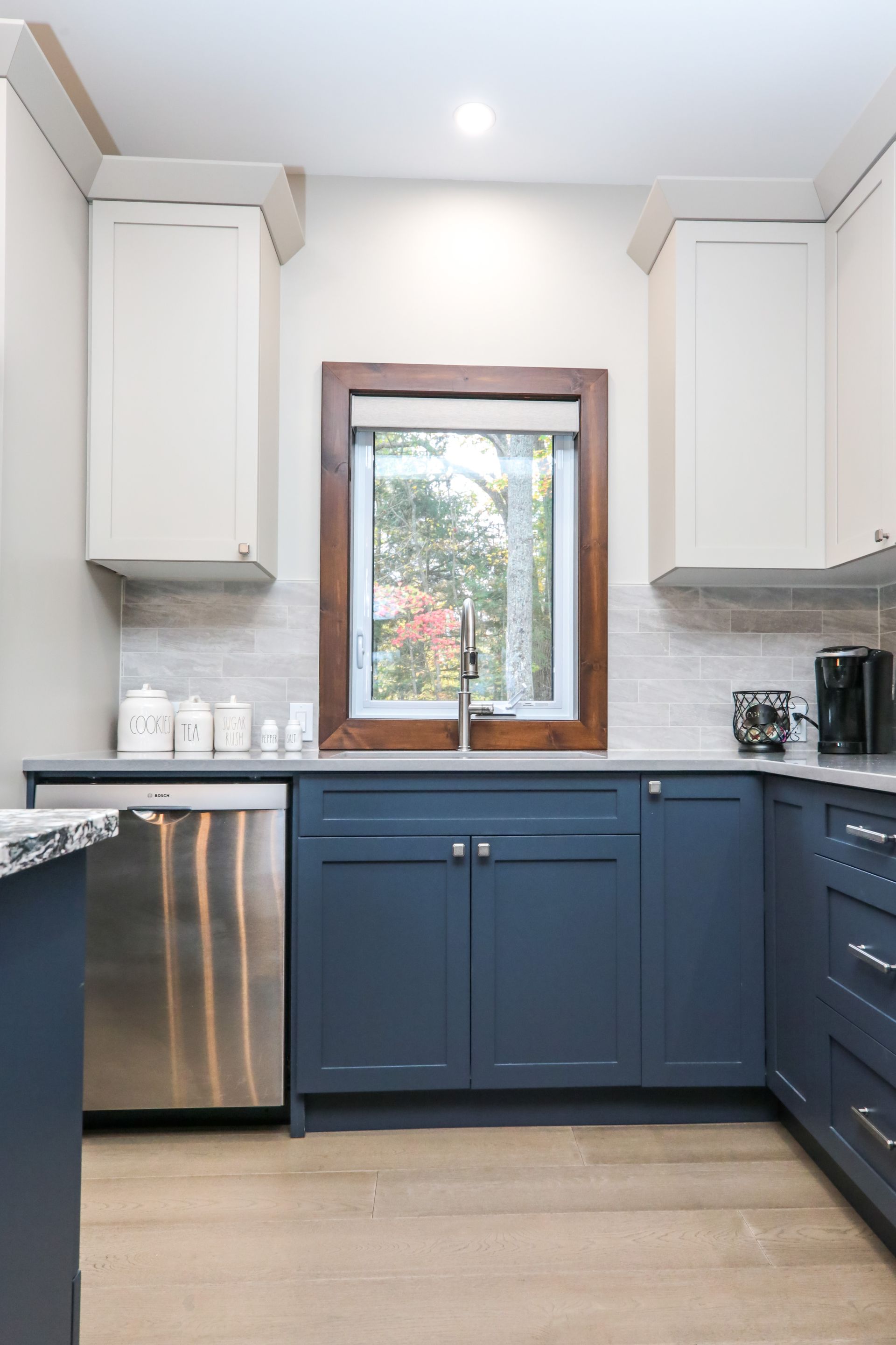 A kitchen with blue cabinets , stainless steel appliances , and a window.
