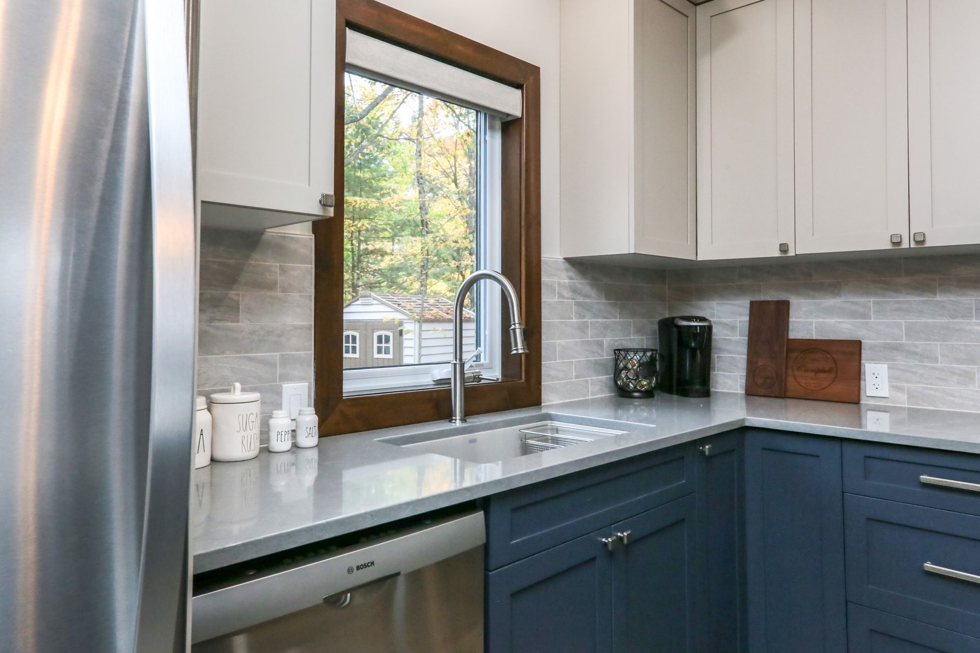 A kitchen with blue cabinets , stainless steel appliances , a sink and a window.