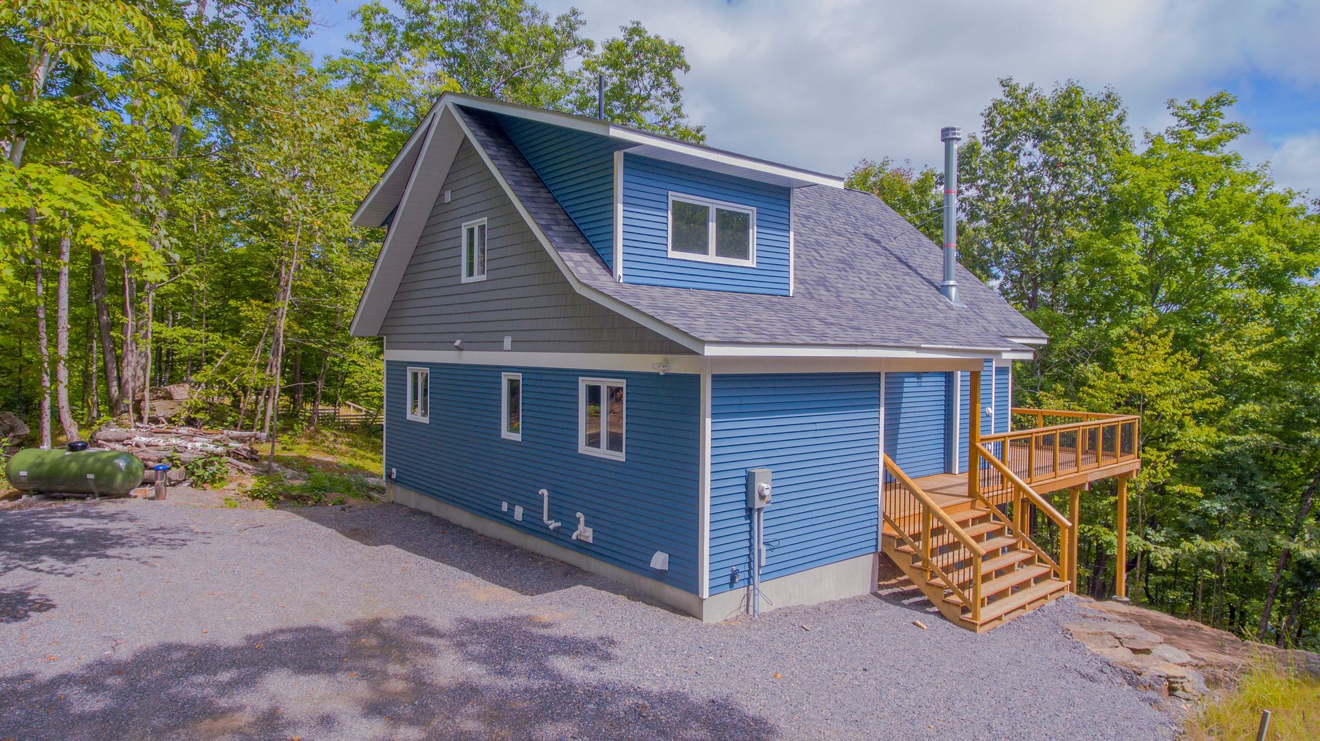 A blue house with a deck is sitting on top of a hill surrounded by trees.
