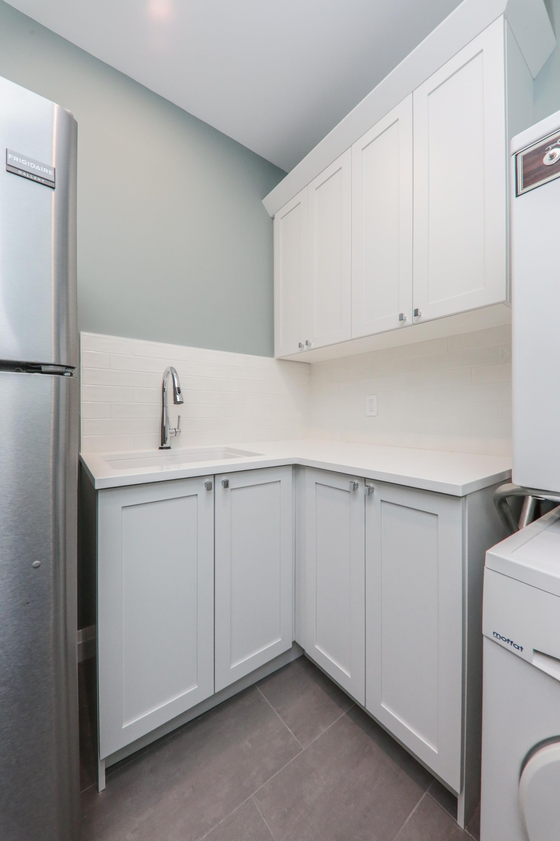 A kitchen with white cabinets and a stainless steel refrigerator