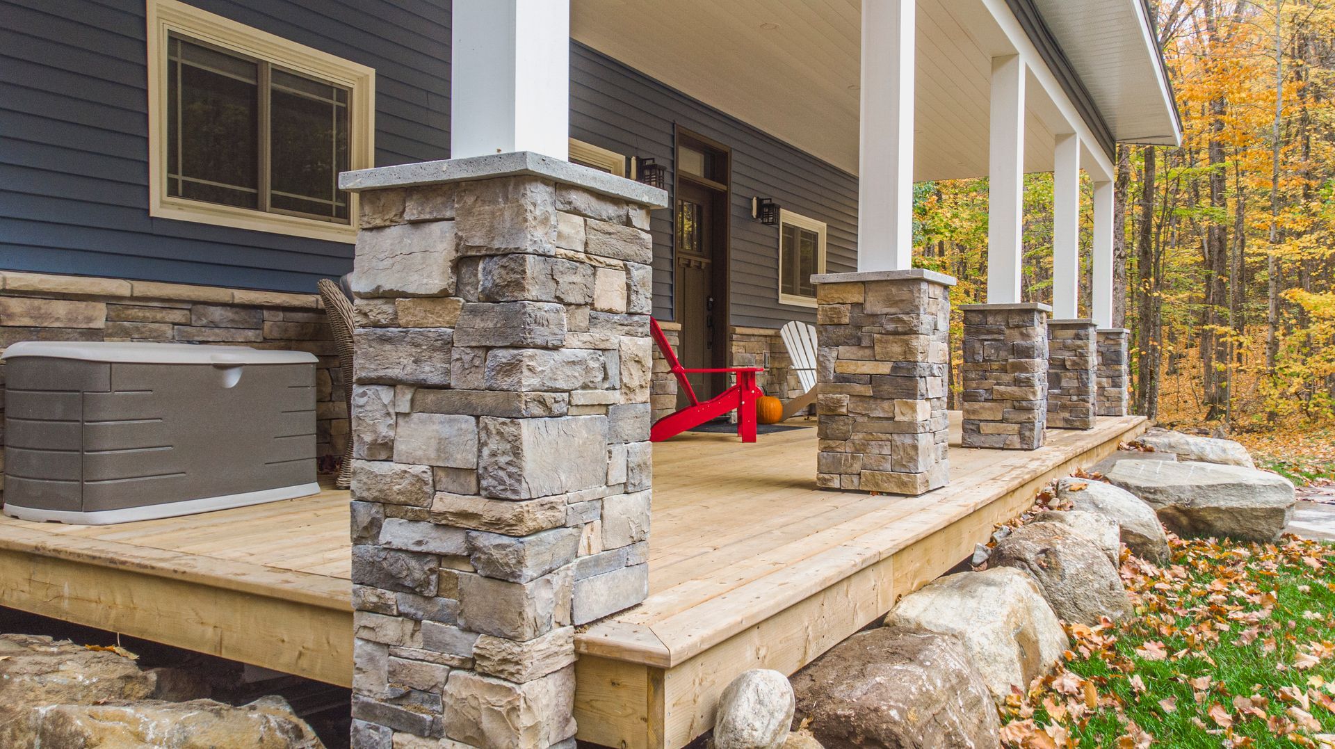 A porch with a wooden deck and stone pillars in front of a house.