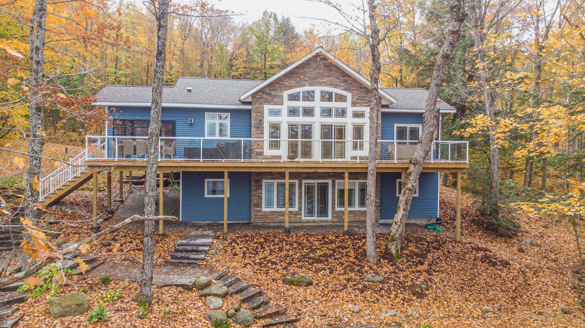 An aerial view of a blue house surrounded by trees in the woods.