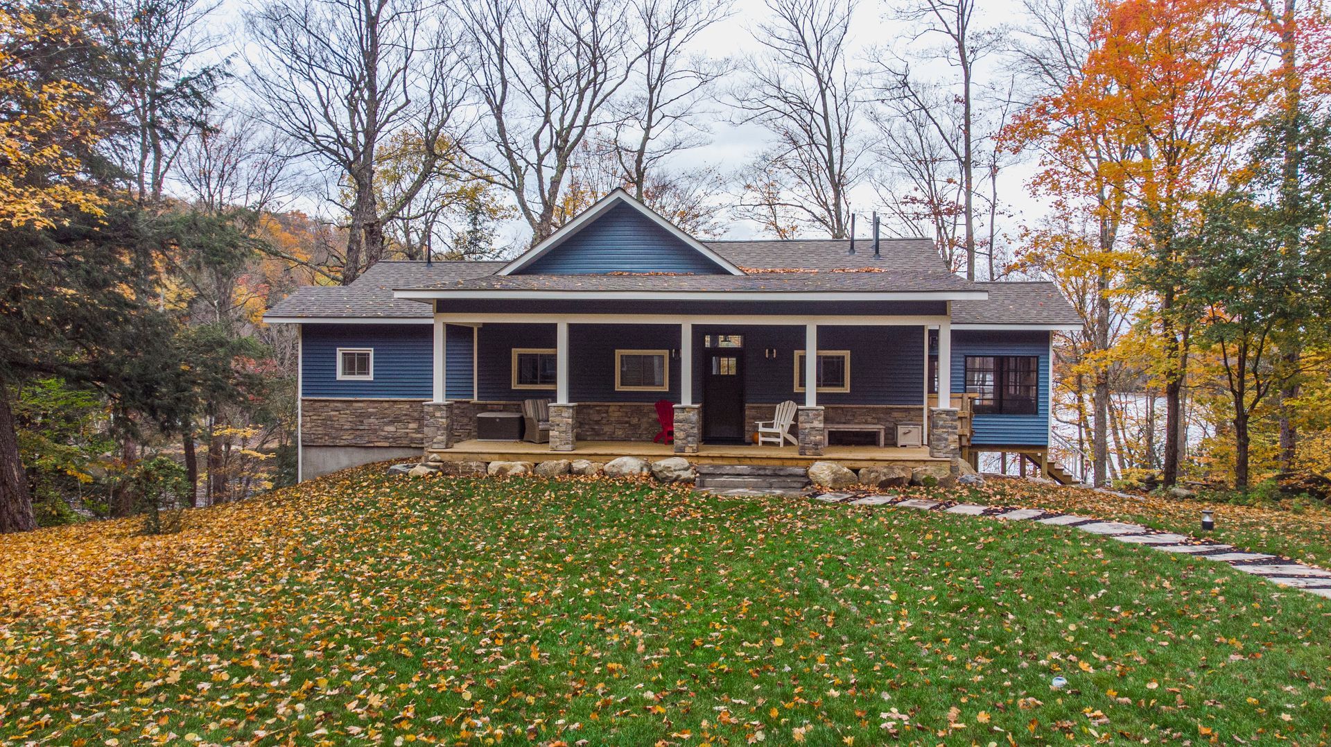 A blue house with a porch in the middle of a lush green field surrounded by trees.