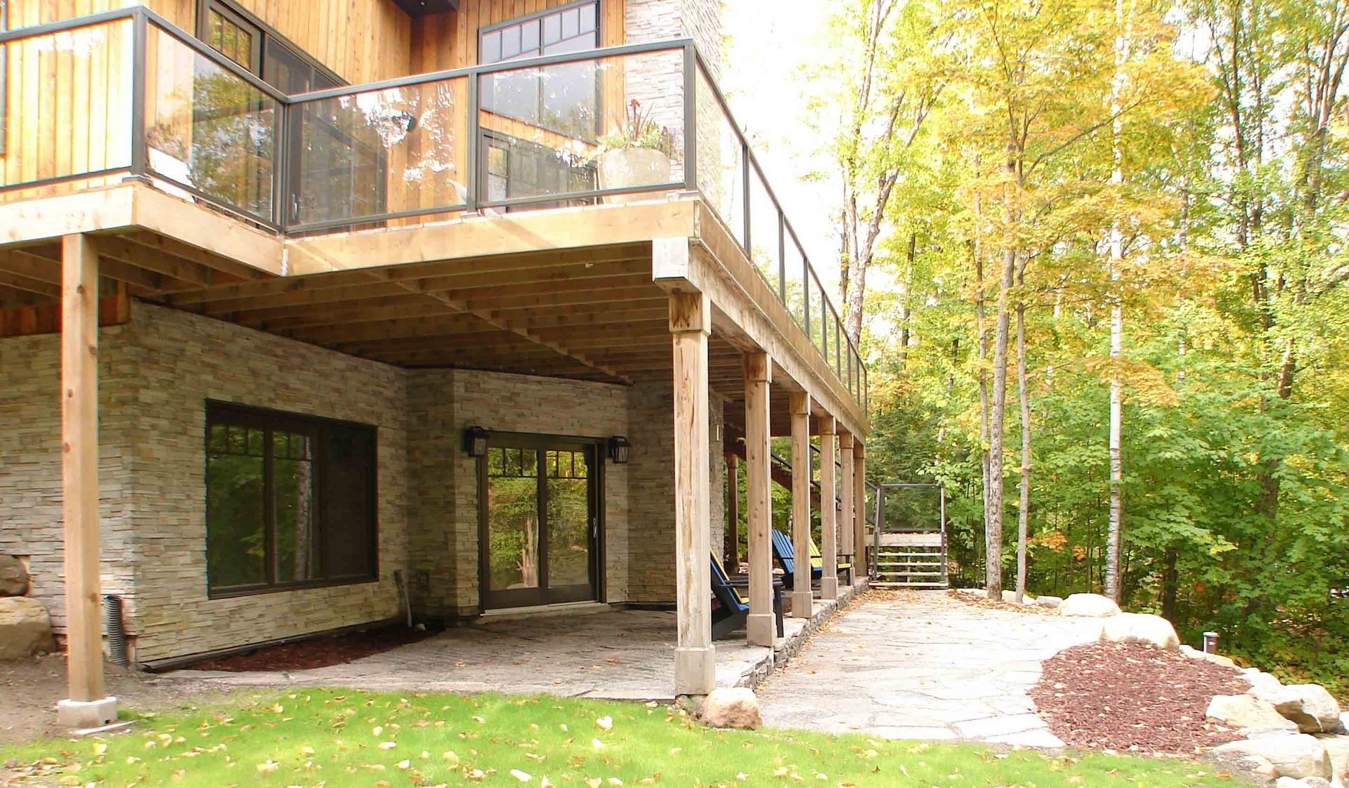 The back of a house with a large deck and patio surrounded by trees.
