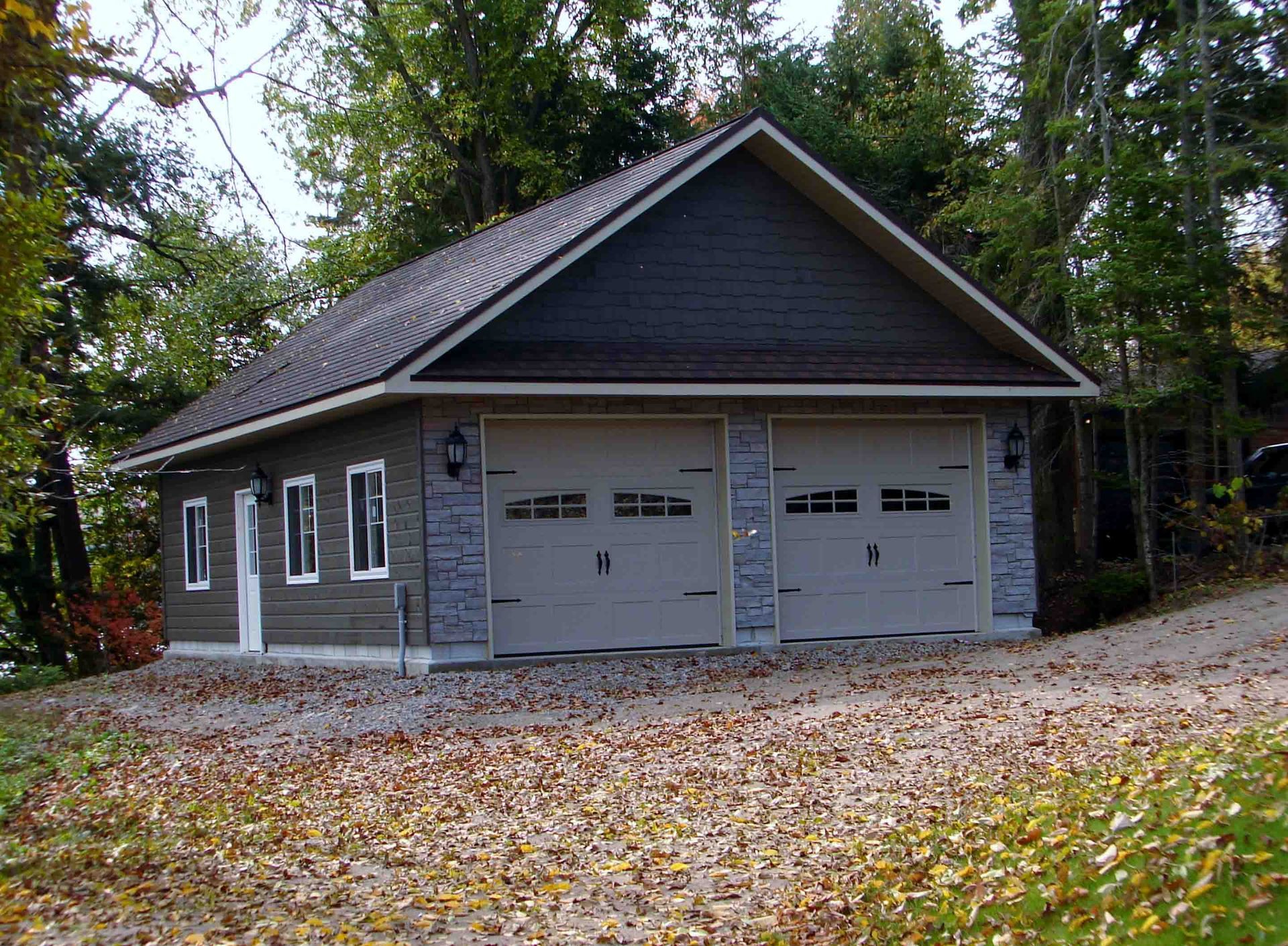 A garage with two garage doors is surrounded by trees and leaves.