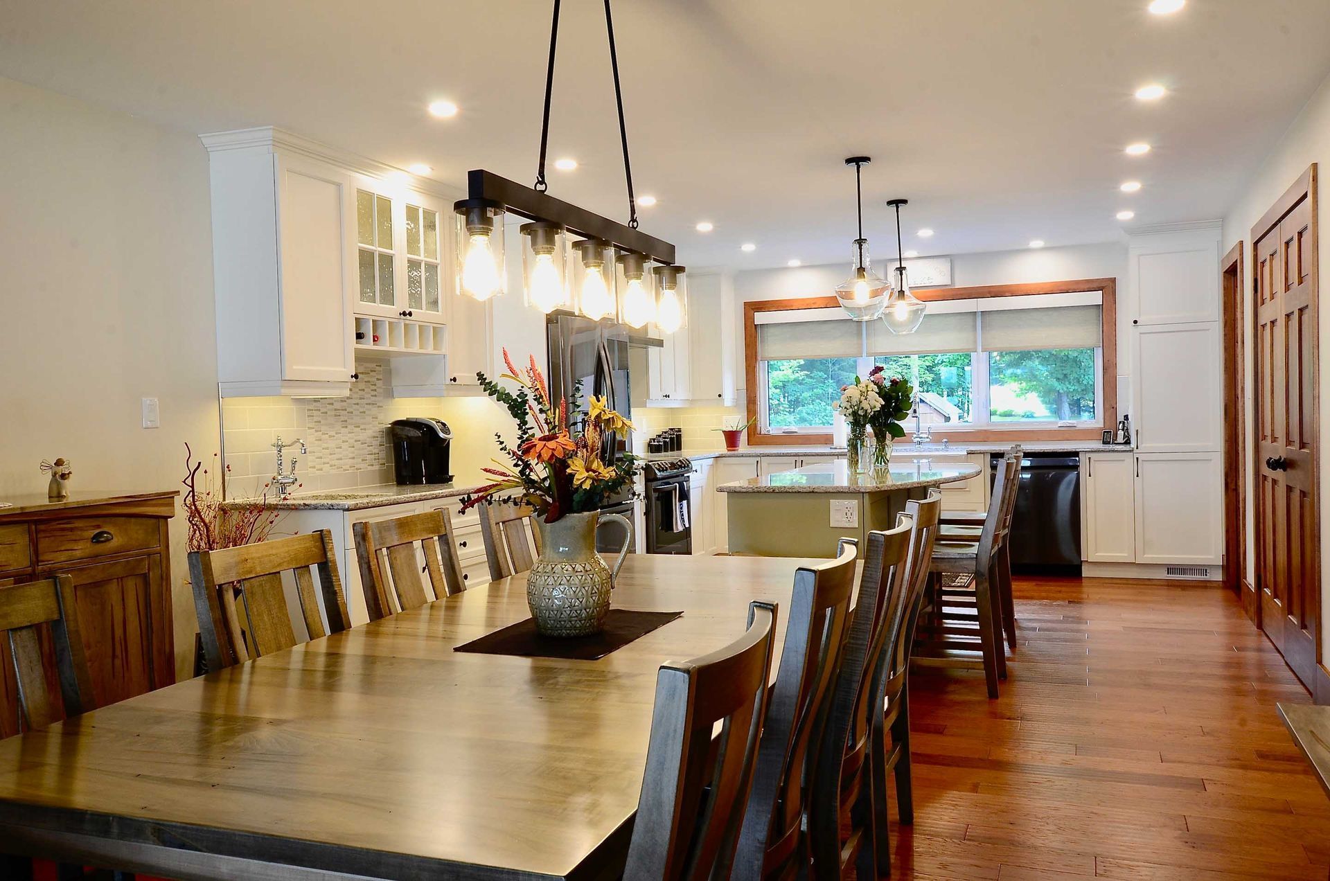 A kitchen with a table and chairs and a vase of flowers on the table.