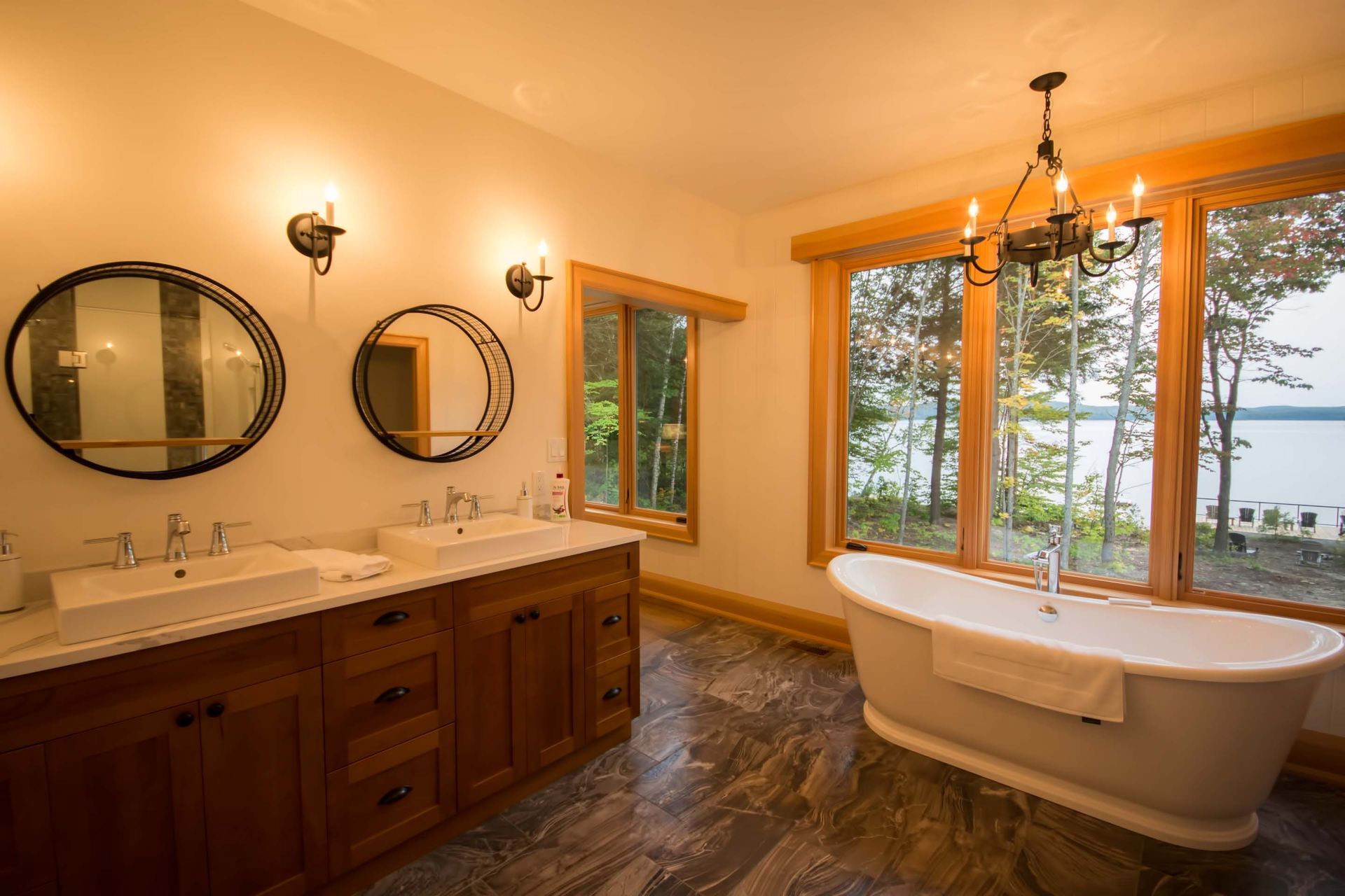 A bathroom with a tub , sinks , mirrors and a view of a lake.