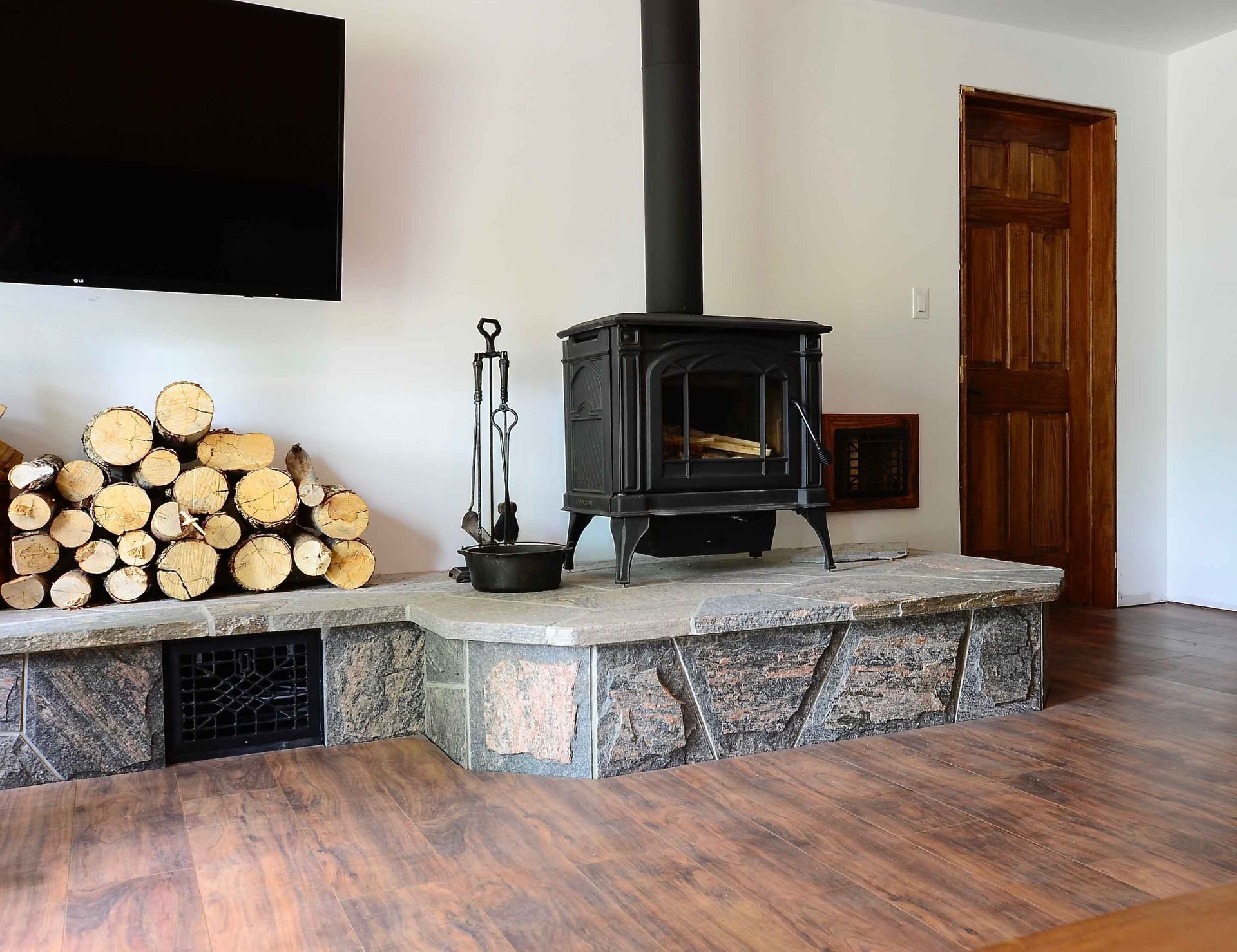 A wood stove is sitting in a living room next to a pile of logs.