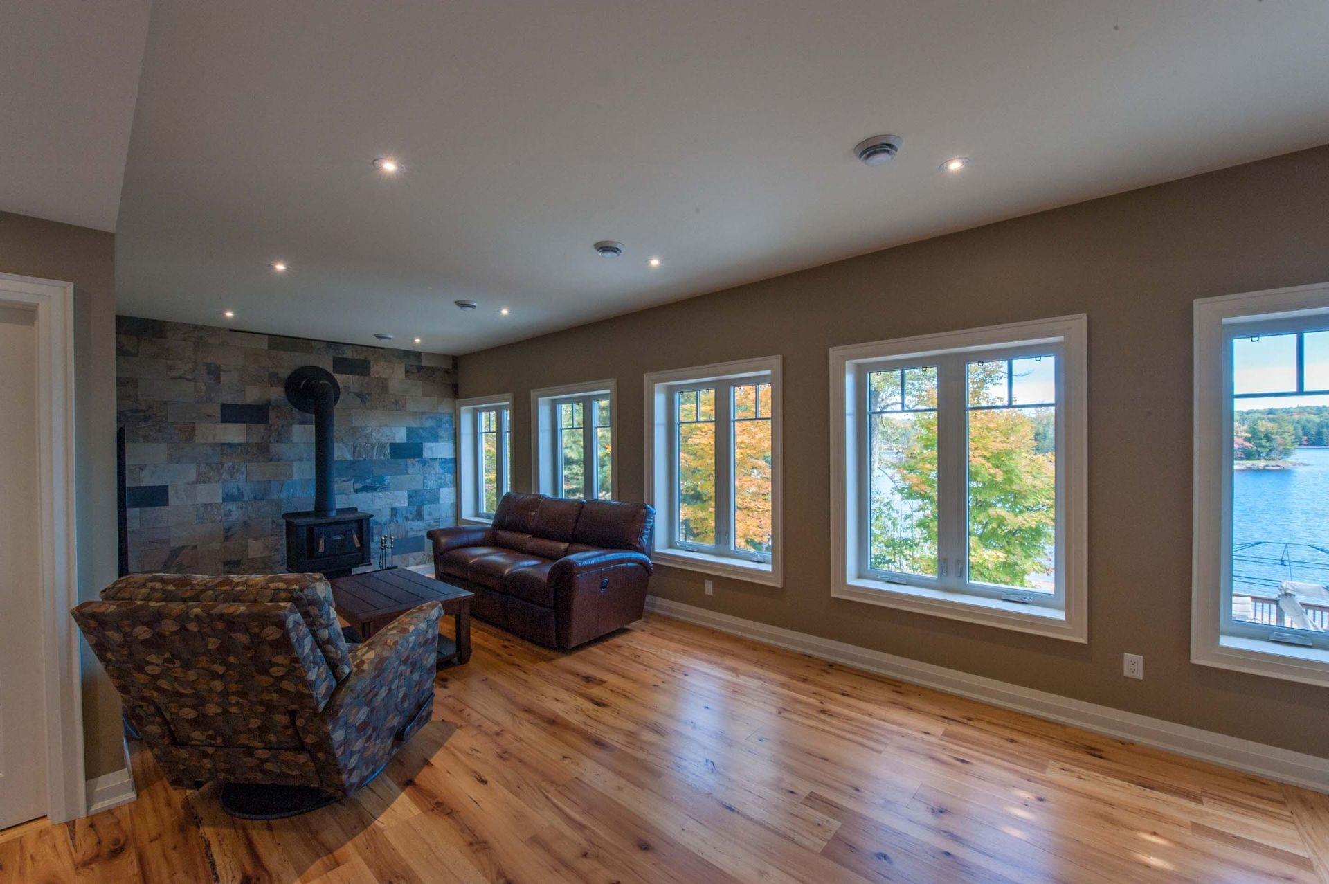 A living room with hardwood floors , a couch , chair and lots of windows.