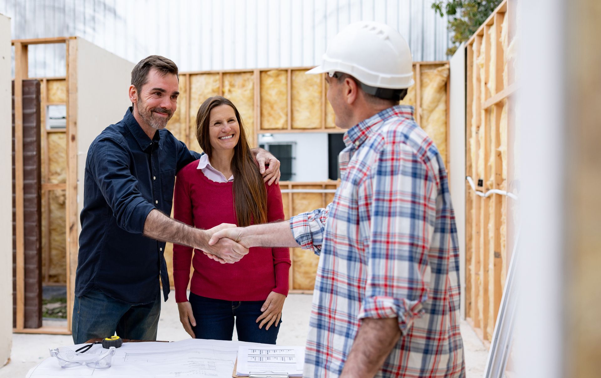 Contractor shakes hands with clients at active build site.