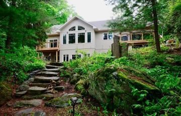 A large house is surrounded by trees and rocks in the middle of a forest.