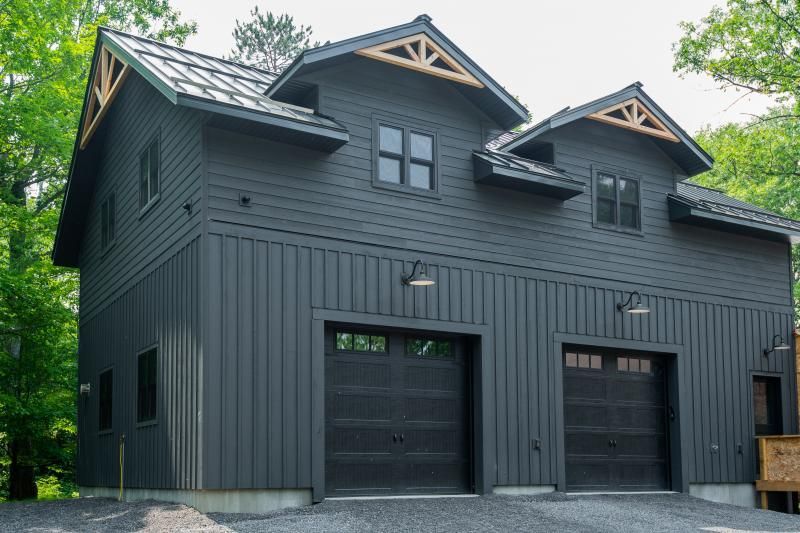 A large black house with three garage doors is surrounded by trees.