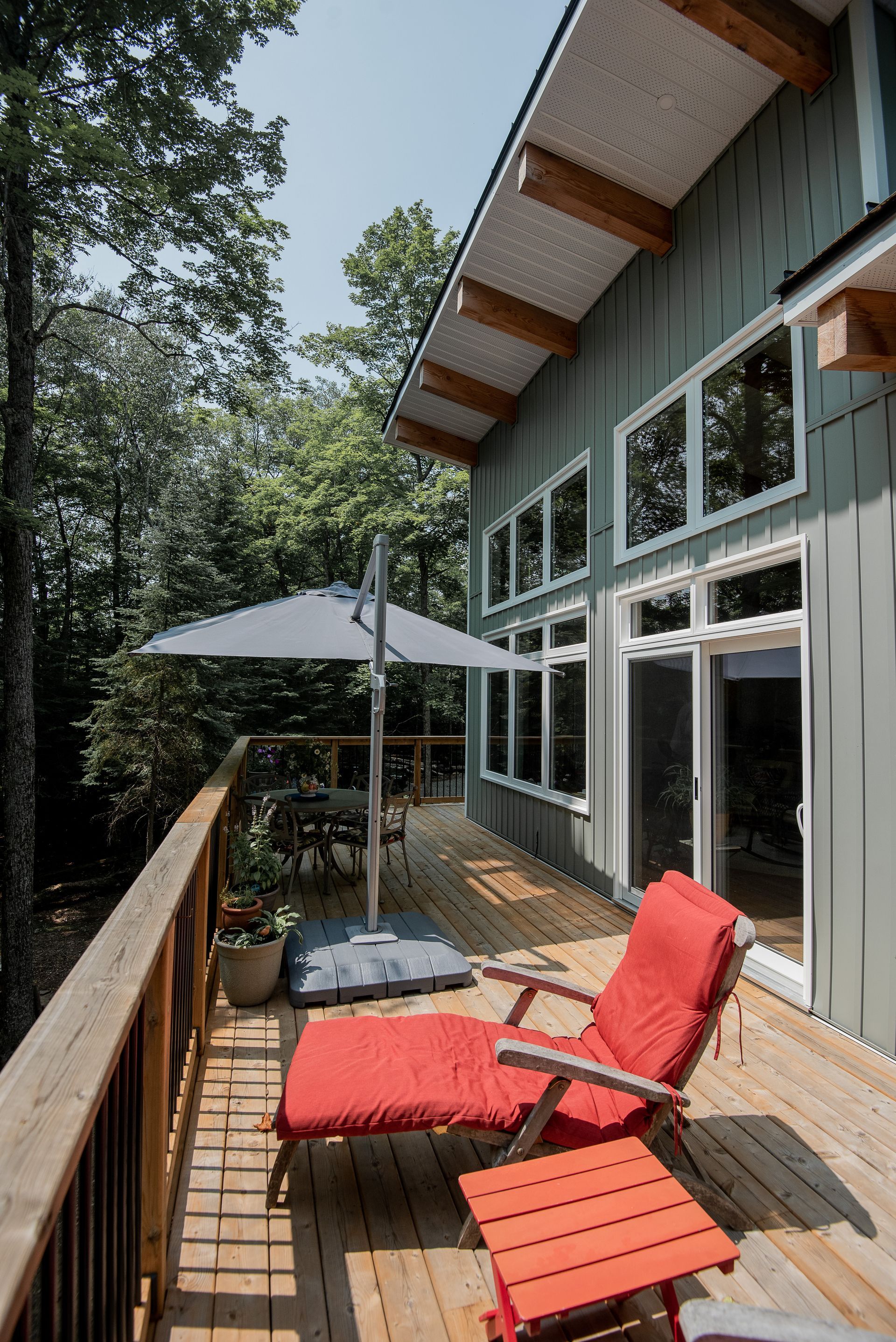 A deck with a red chair , ottoman , umbrella and table.