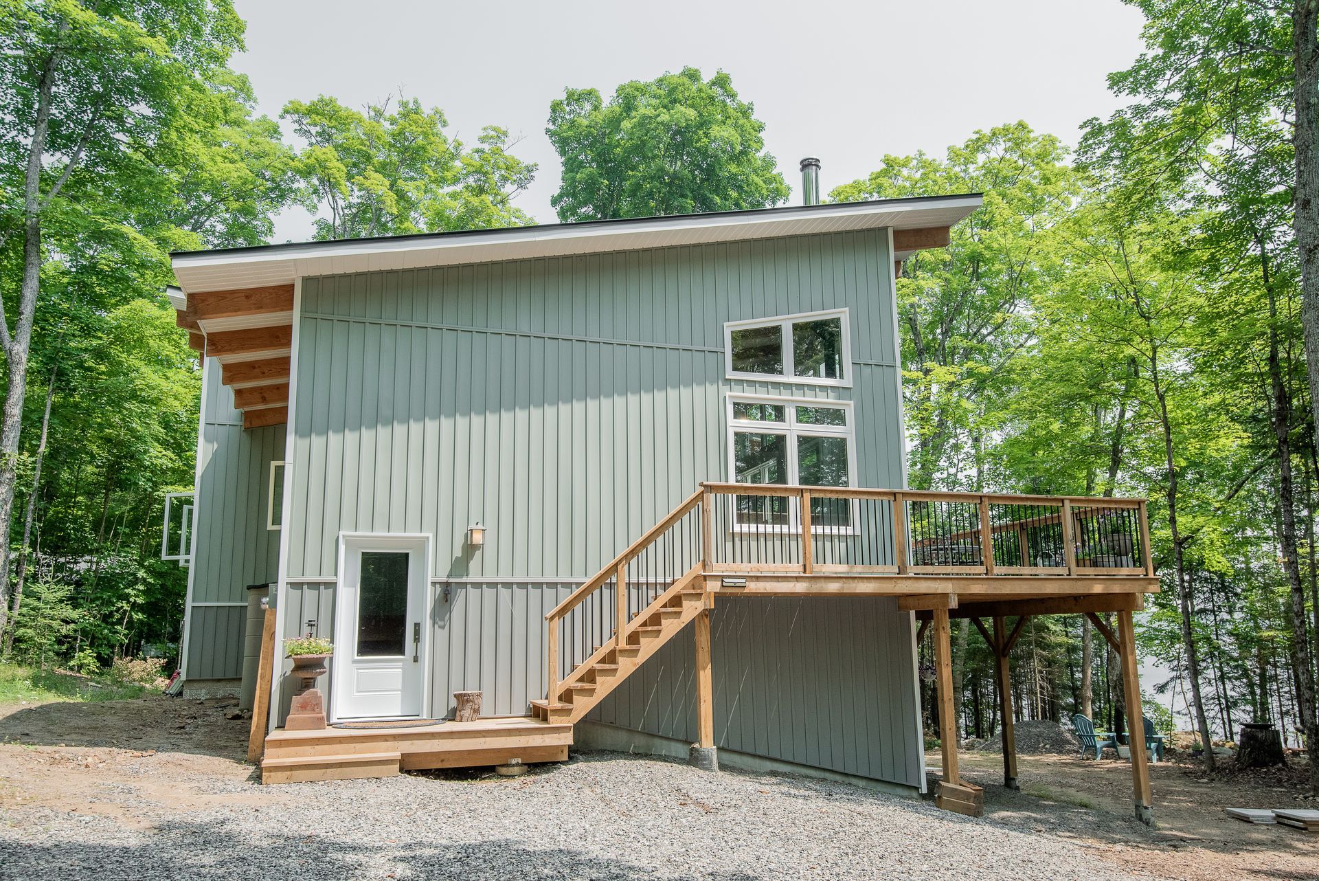 A small house with a wooden deck and stairs in the woods.