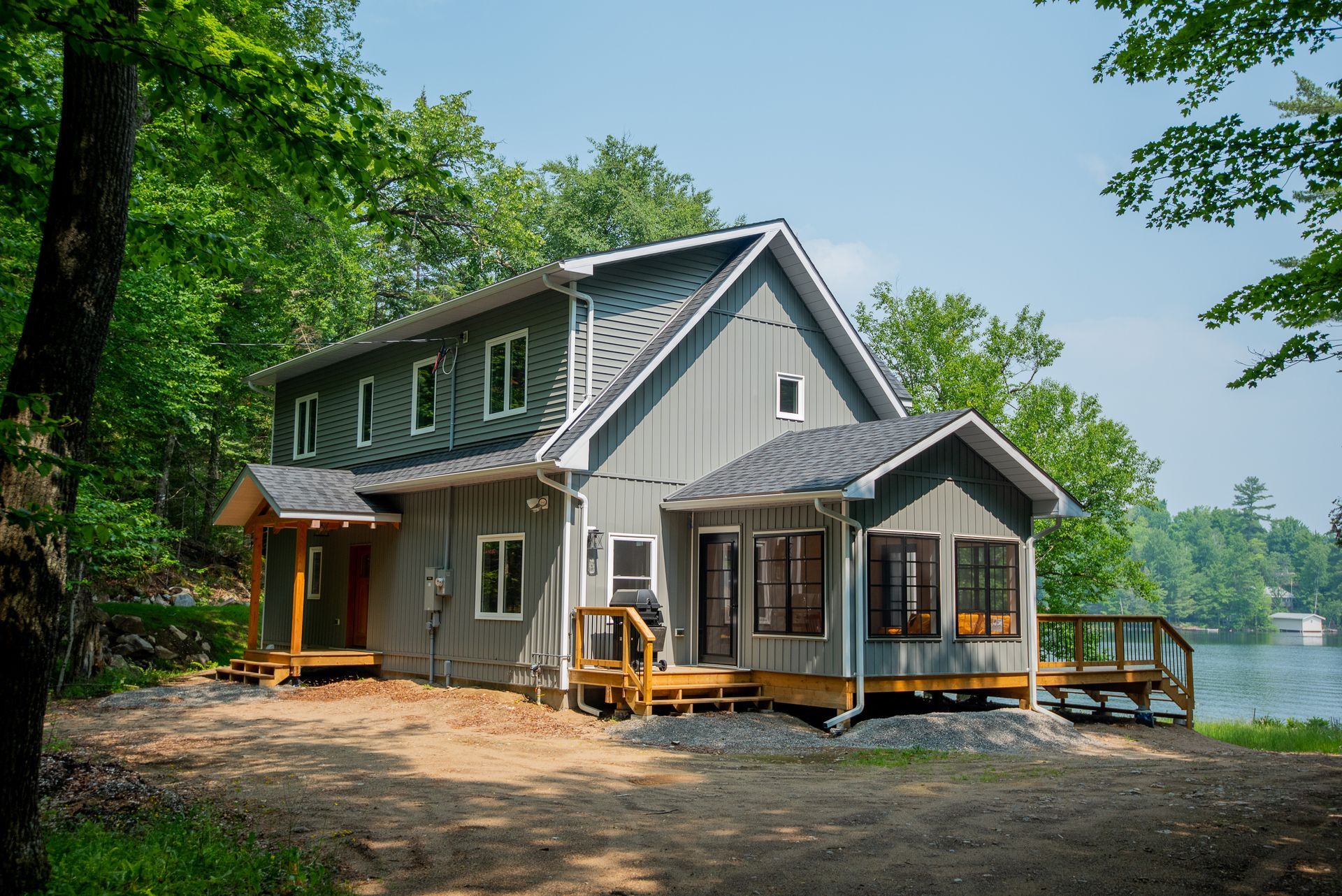 A large gray house is sitting next to a lake surrounded by trees.