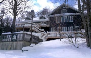 A large house with stairs leading up to it is covered in snow.