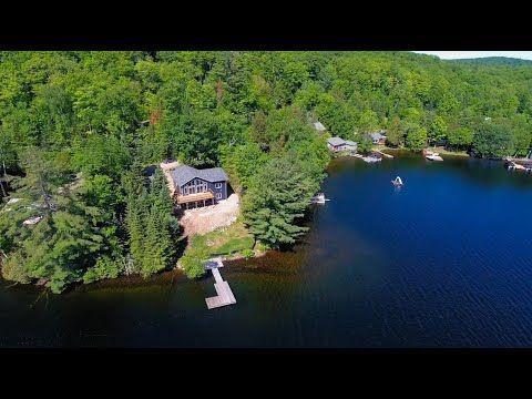 An aerial view of a house on the shore of a lake surrounded by trees.