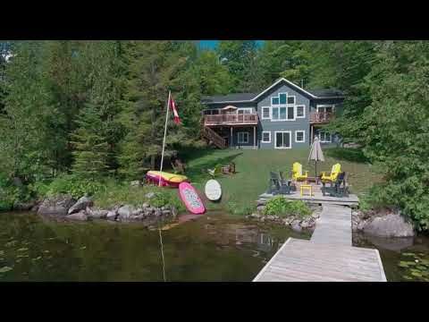 An aerial view of a house on a lake with a dock and kayaks.