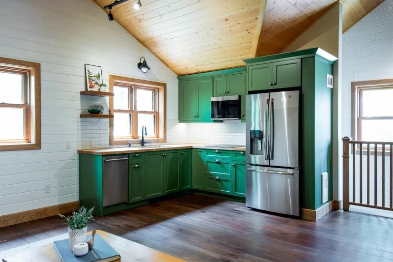 A kitchen with green cabinets and a stainless steel refrigerator.