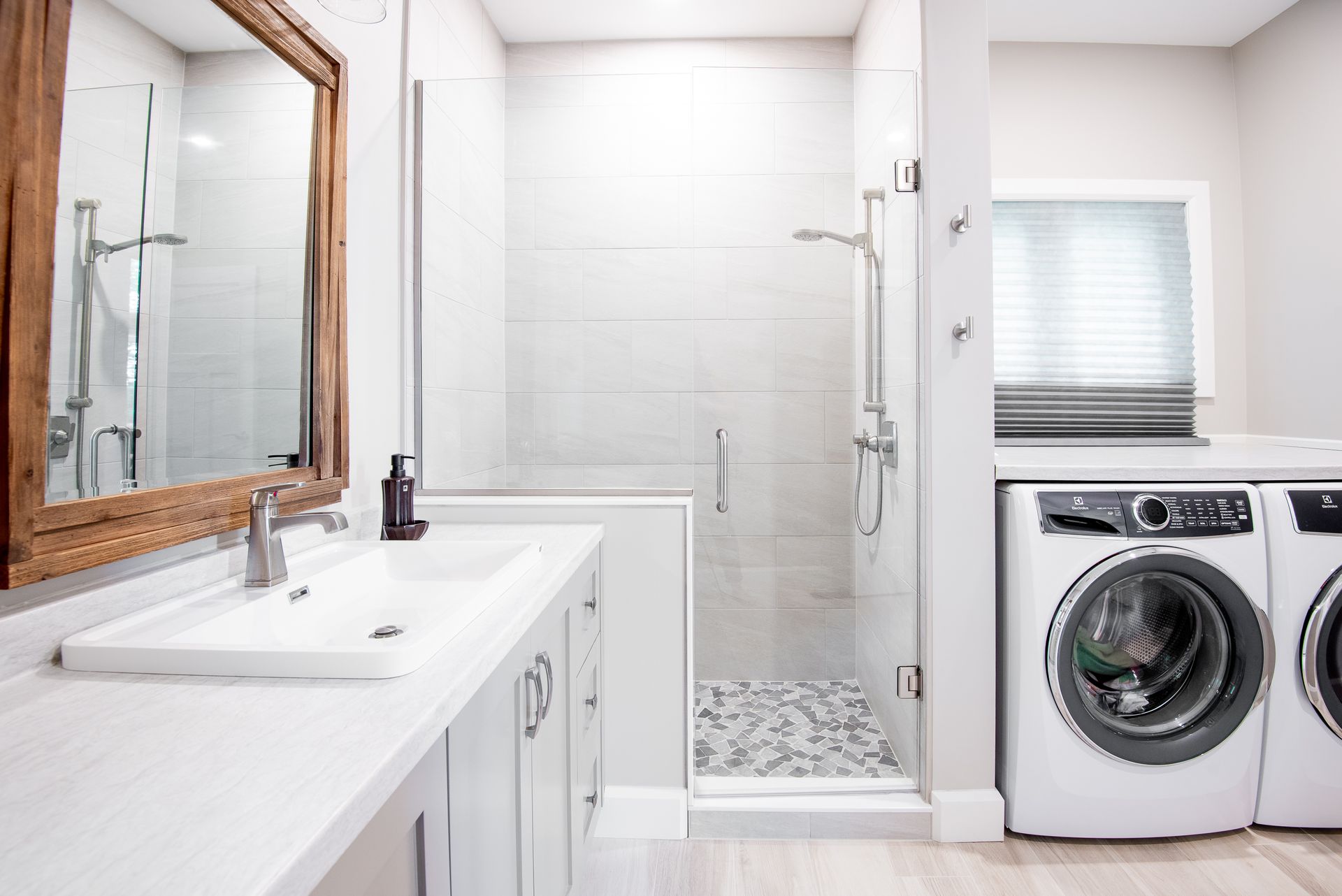 A bathroom with a sink , washer and dryer , and a walk in shower.