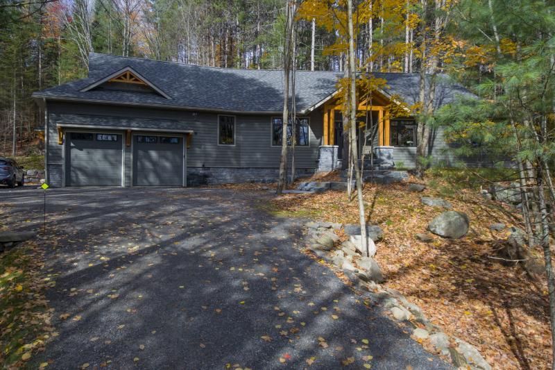A house in the middle of a forest with a driveway leading to it.