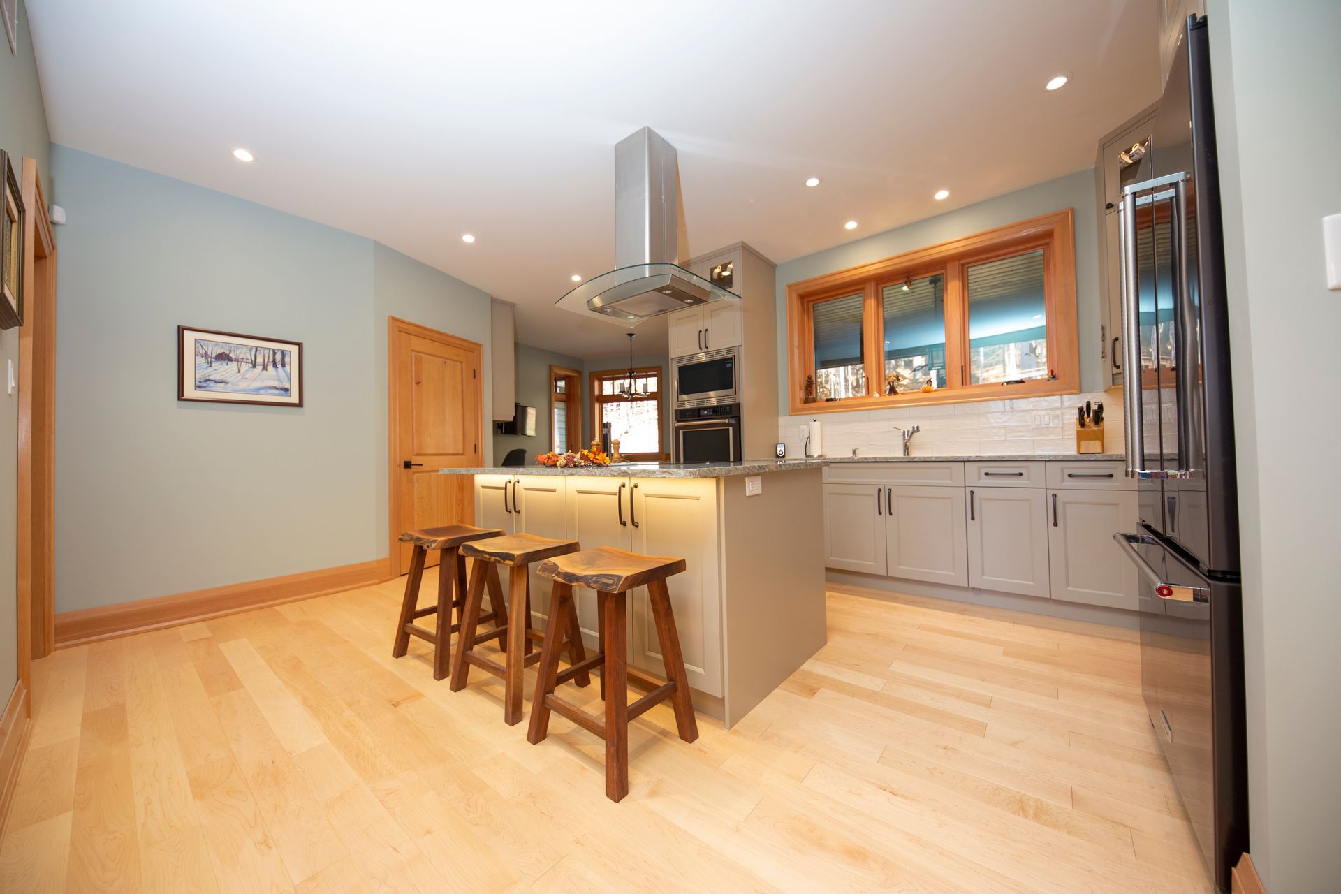 A kitchen with a large island , stools and a refrigerator.