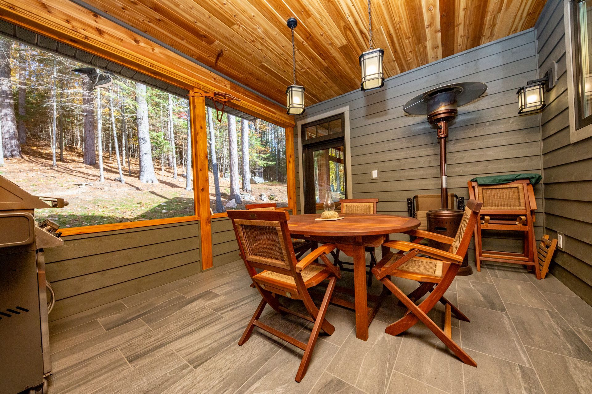 A screened in porch with a table and chairs and a heater.