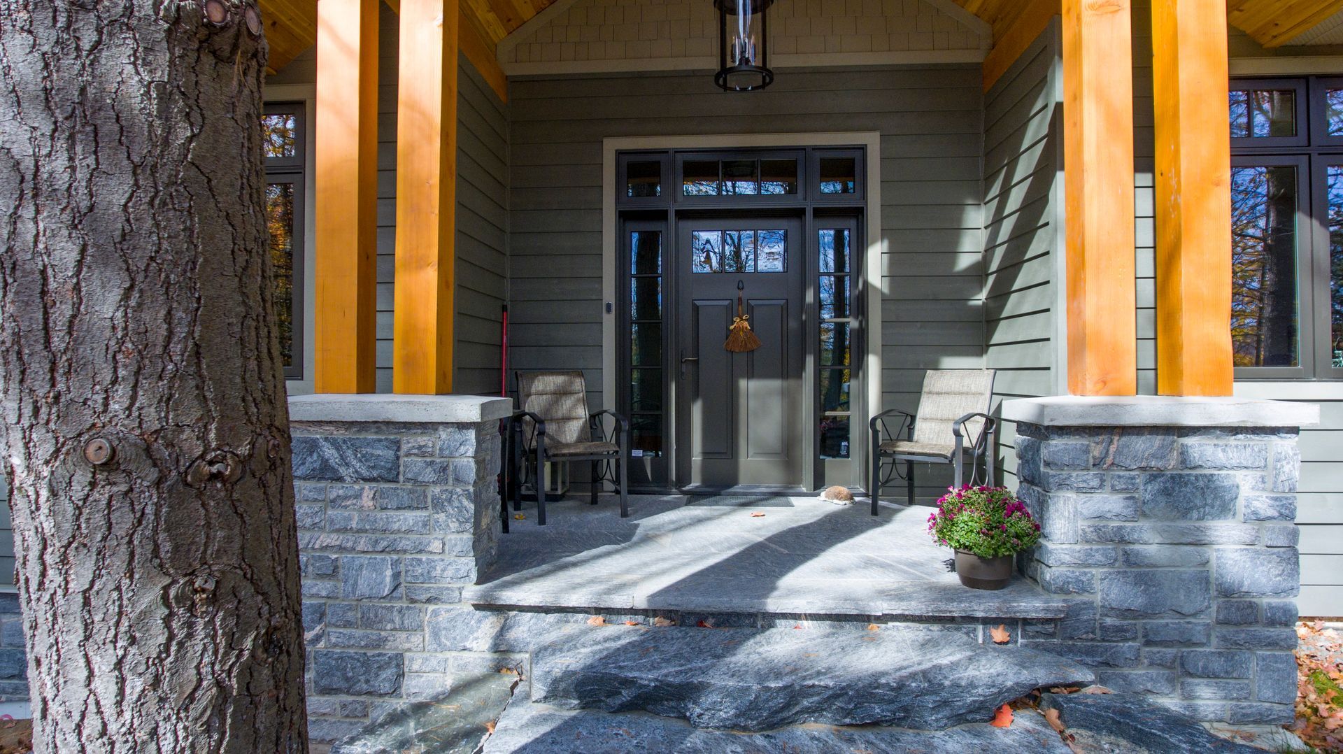 The front porch of a house with a tree in the foreground.