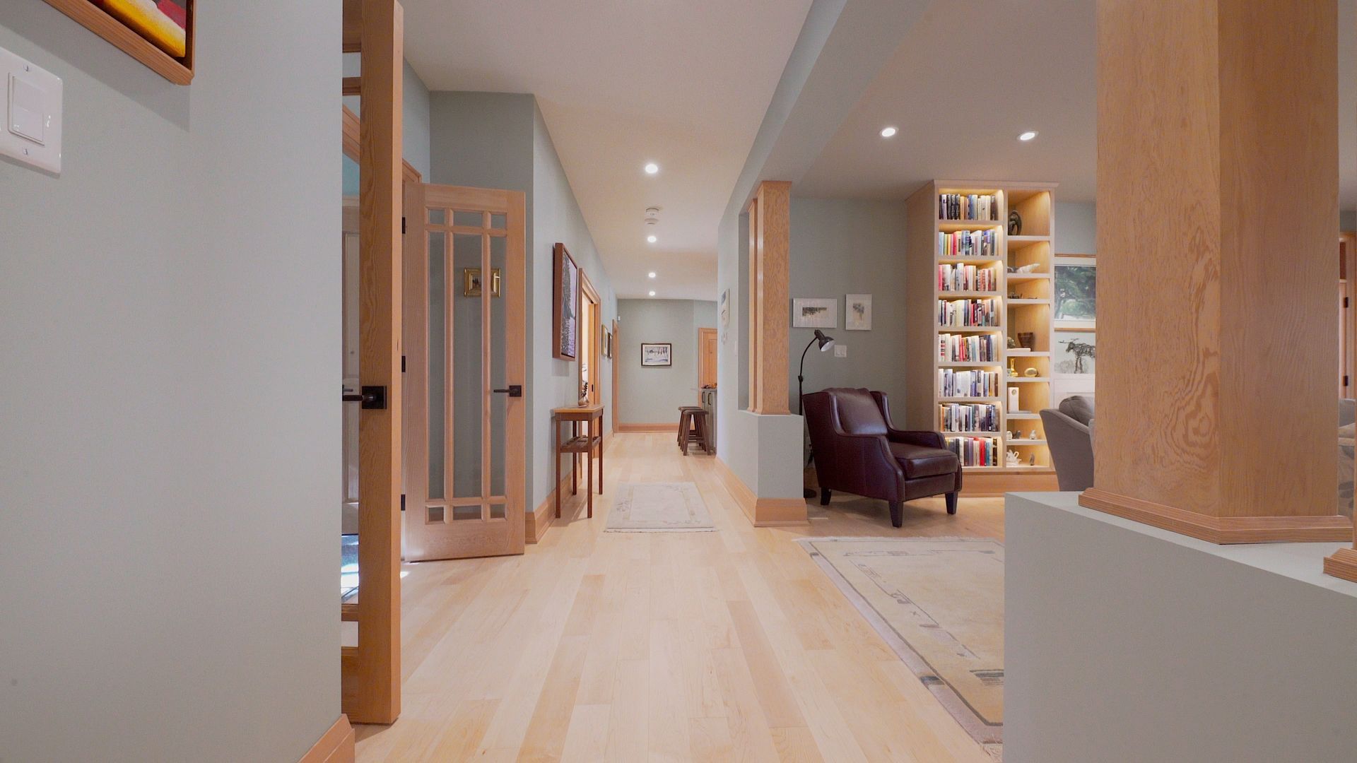 A hallway in a house with hardwood floors and a bookshelf.
