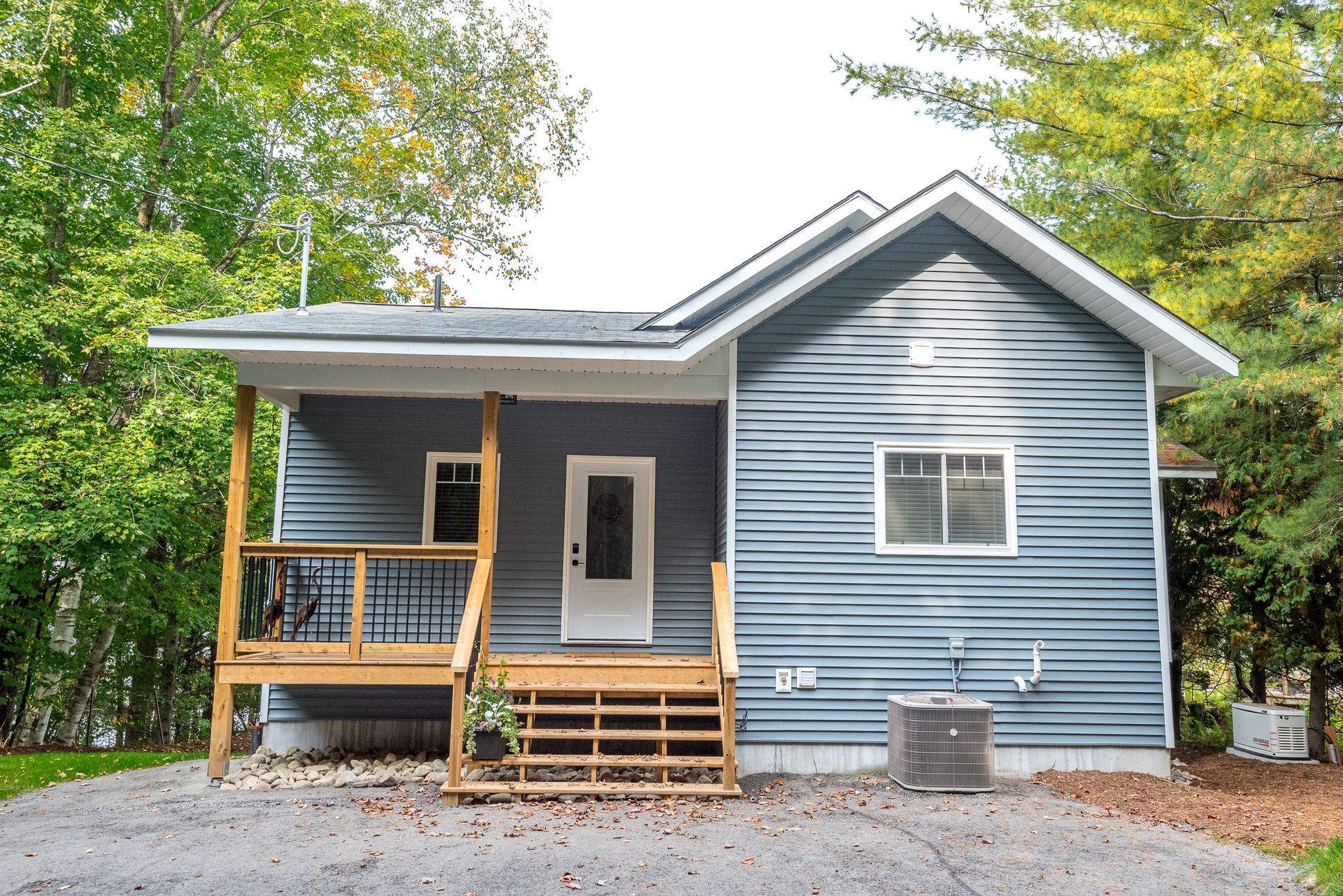 A small blue house with a porch and trees in the background