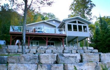 A large house is sitting on top of a rocky hill surrounded by trees.
