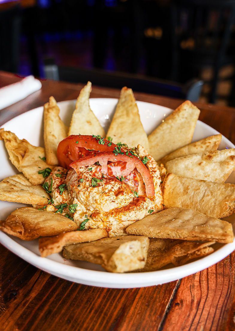 A white plate topped with hummus and pita chips on a wooden table.