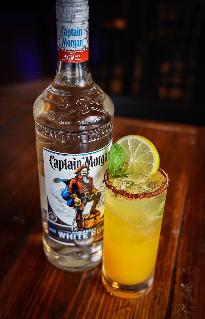 A bottle of captain morgan rum and a glass of orange juice on a wooden table.