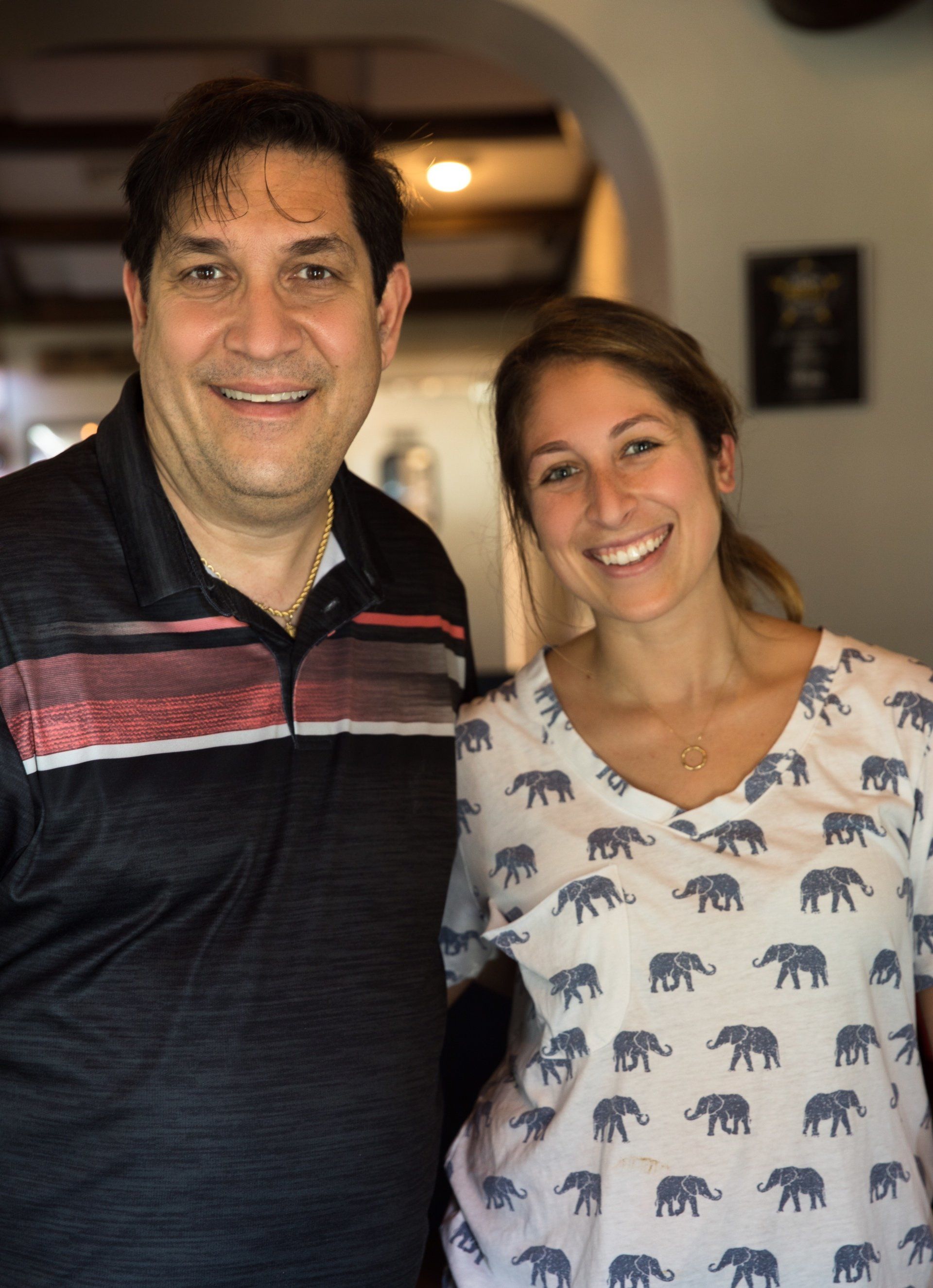 A man and a woman are posing for a picture and the woman is wearing an elephant shirt.
