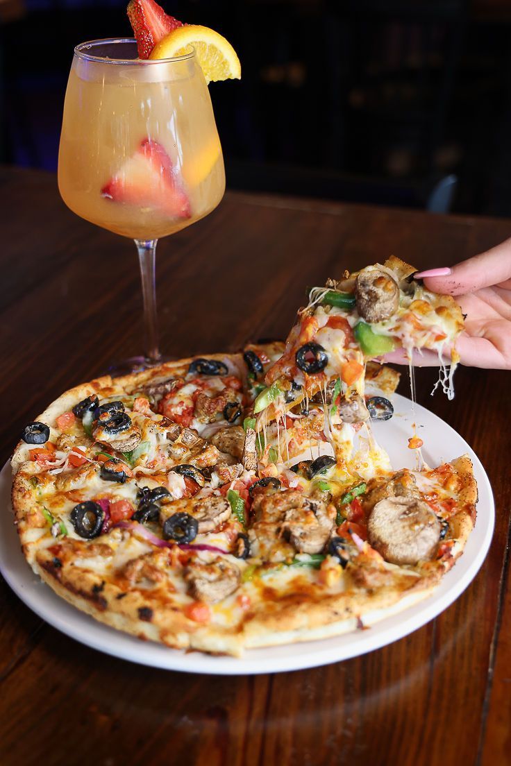 A person is taking a slice of pizza from a plate next to a glass of wine.