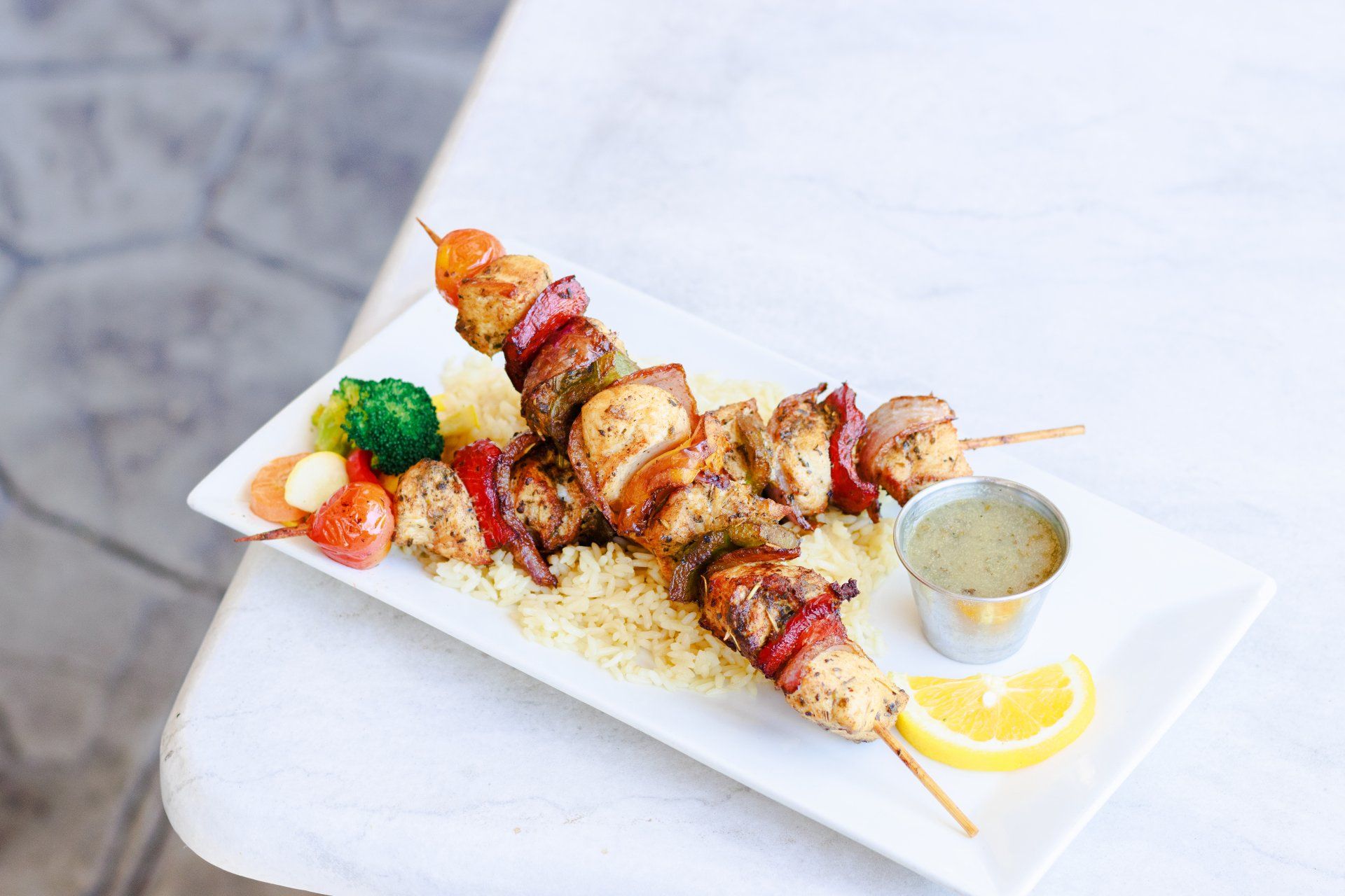 A white plate topped with chicken skewers and rice on a table.