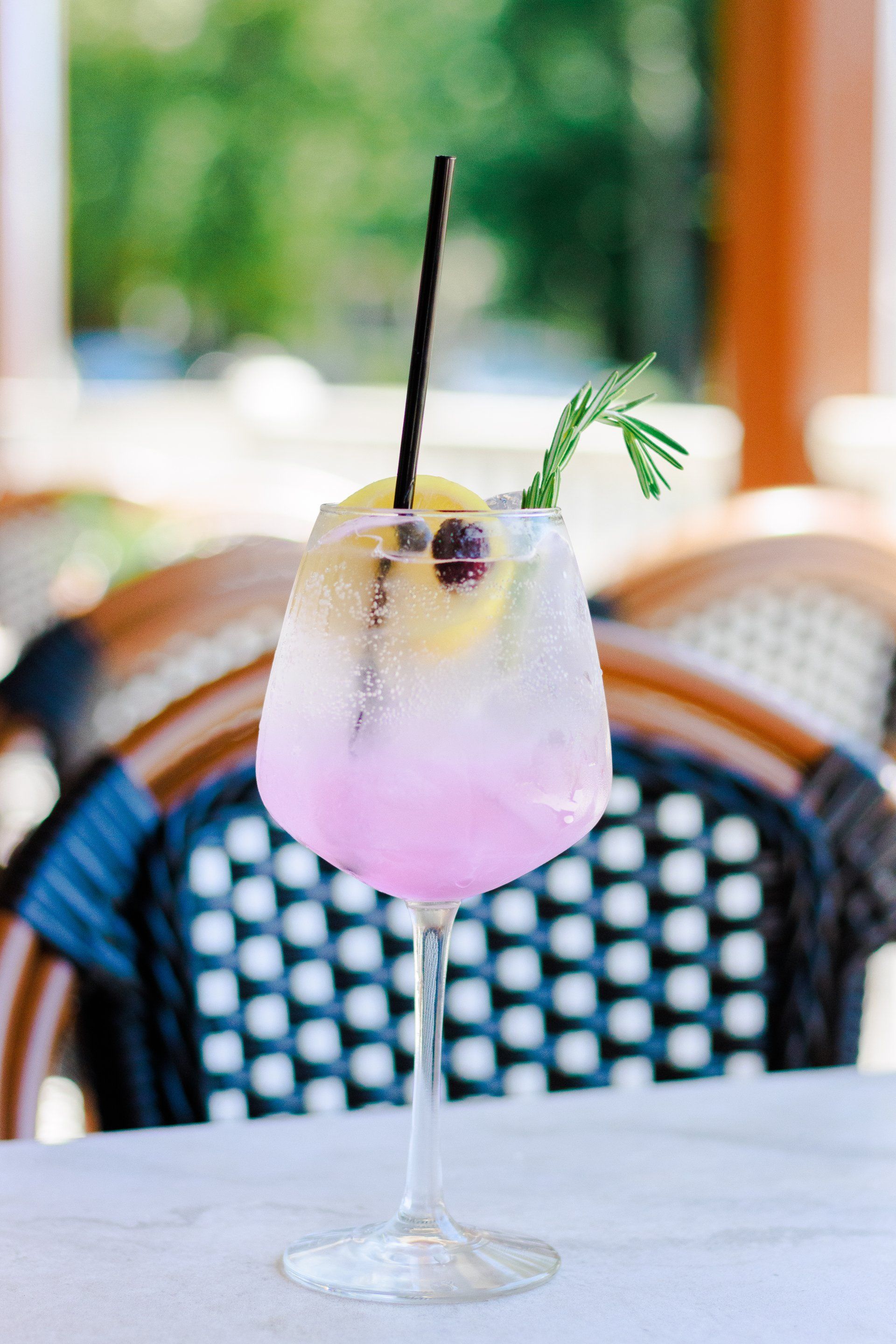 A close up of a pink cocktail in a wine glass on a table.