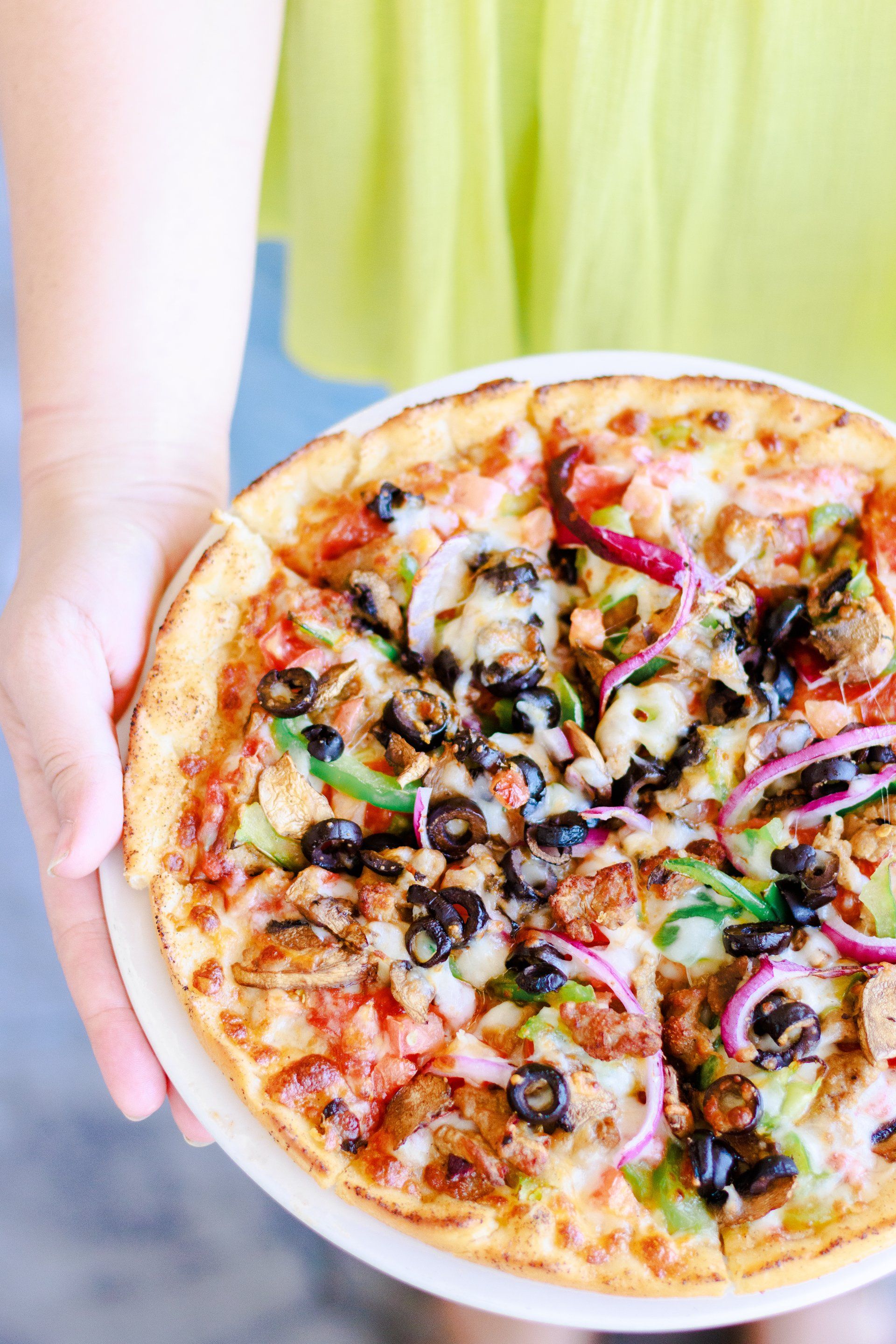 A person is holding a white plate with a pizza on it.