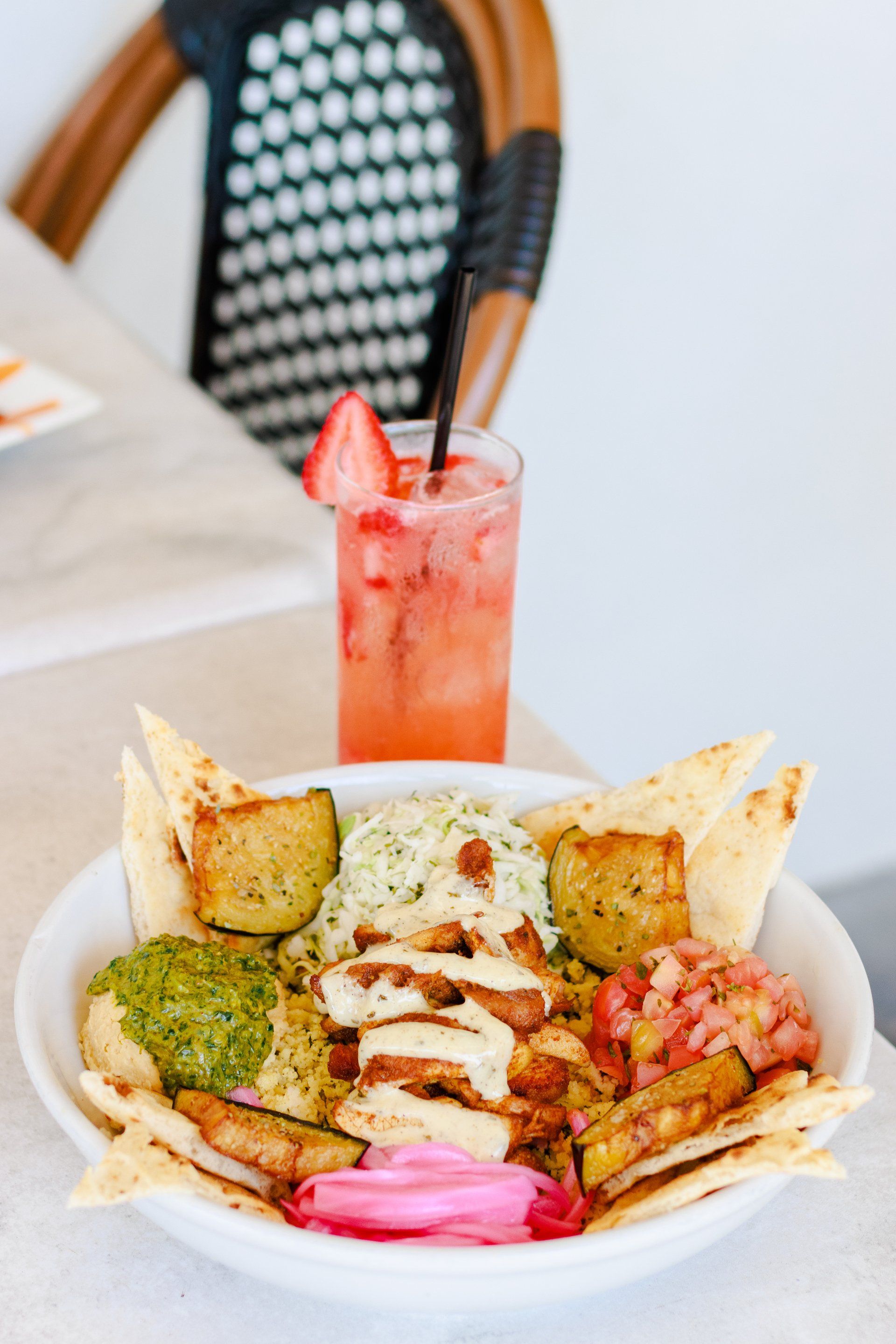 A bowl of food with a drink in the background on a table.