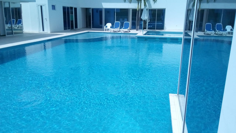 Piscina de agua turquesa frente a un edificio blanco con camastros.